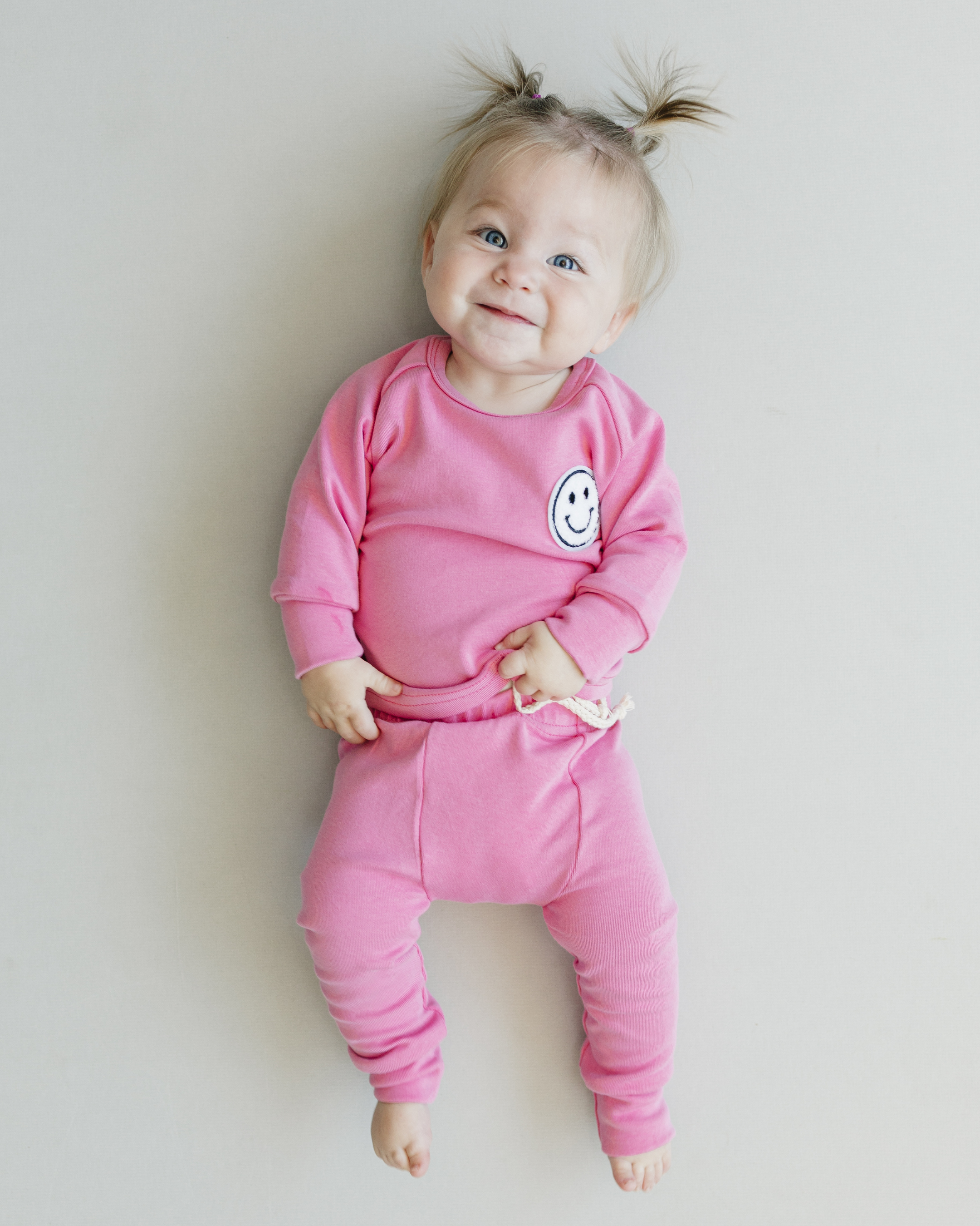 Baby girl in pink lounge set smiley bubble gum, featuring a soft tee and matching pants with a smiley patch.