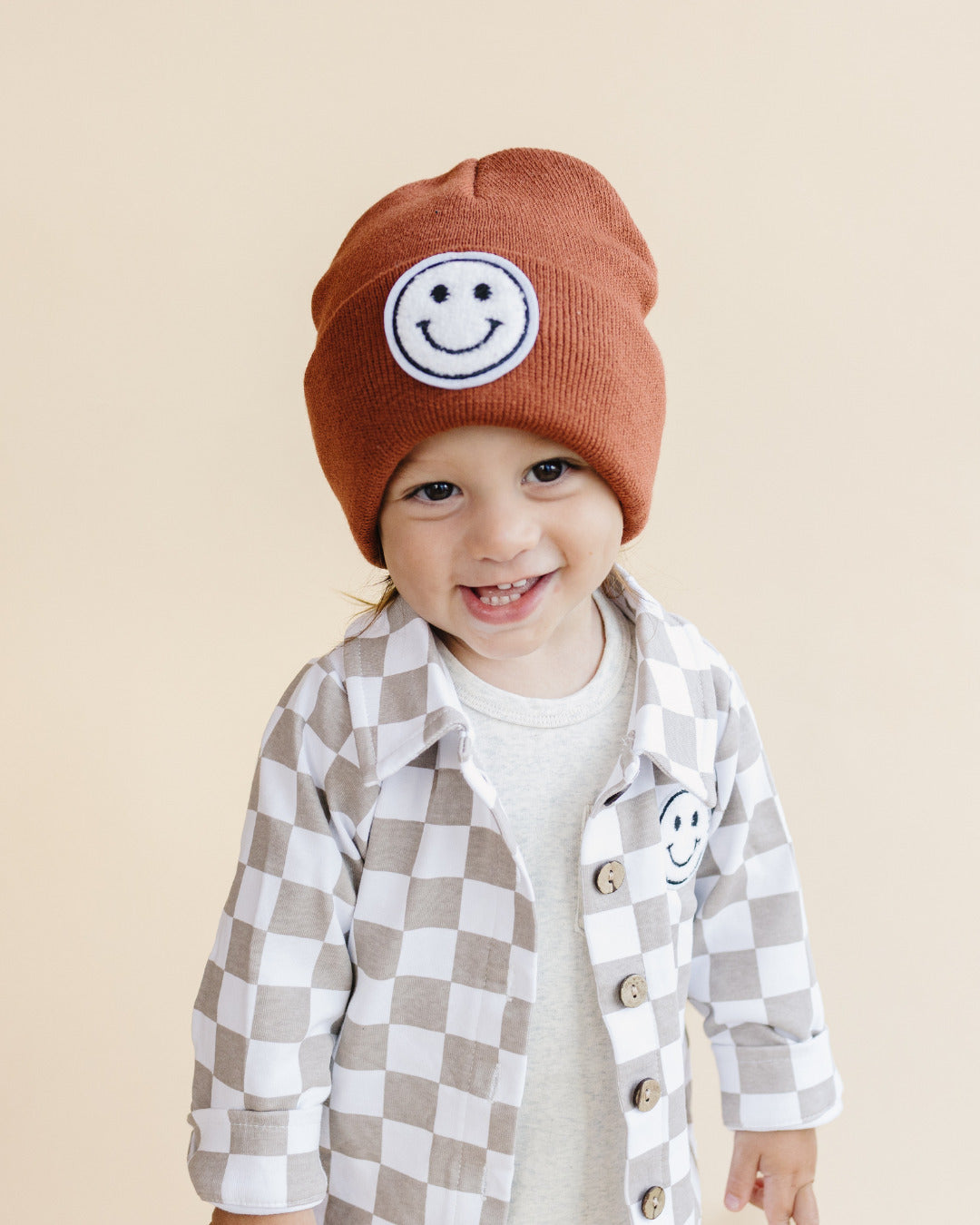 Child smiling in a cozy Cotton Shacket with a smiley patch and beanie, showcasing playful stylish fashion.