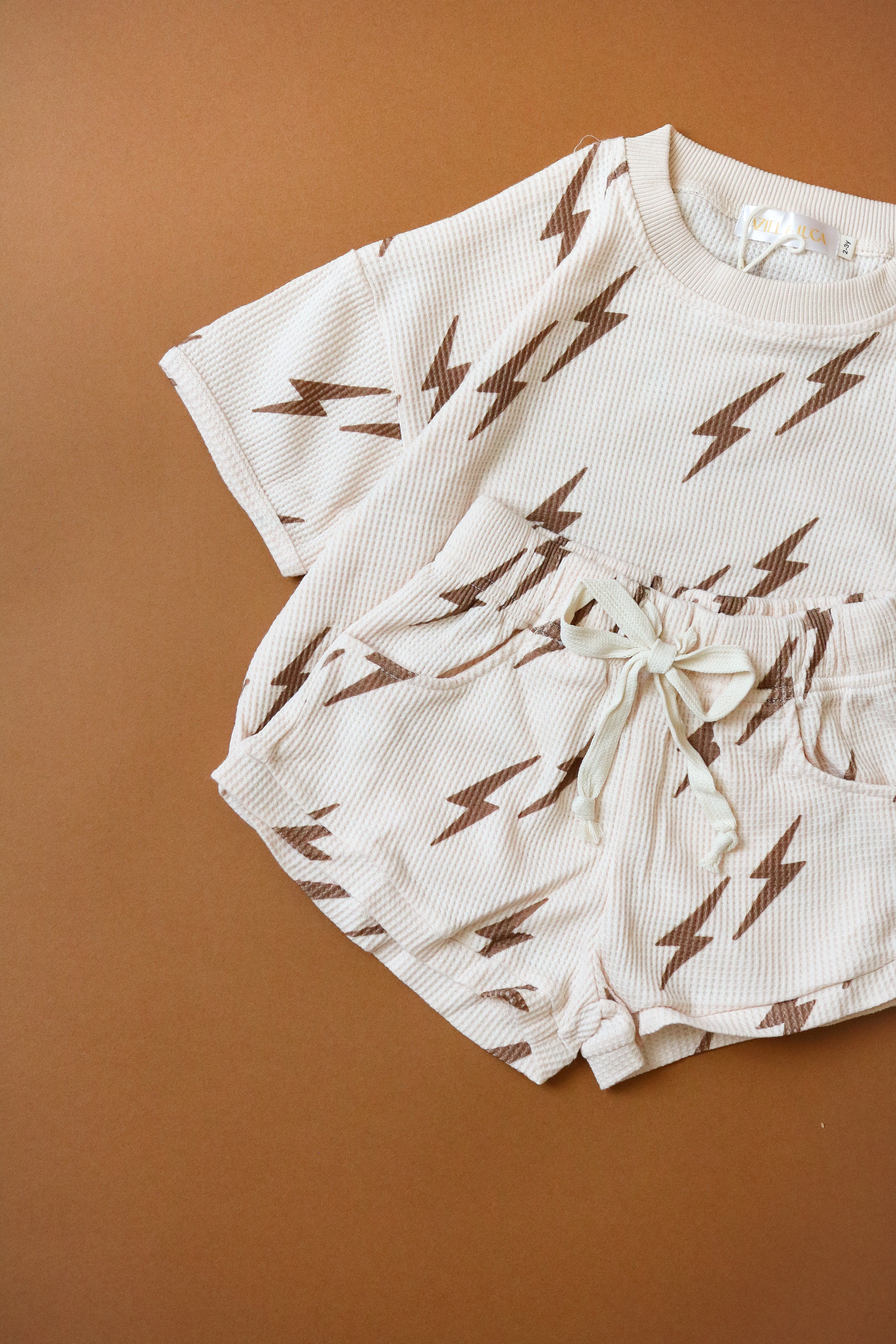 Printed waffle sets kids in lightning bolt design, featuring comfy tee and shorts for summer fun.
