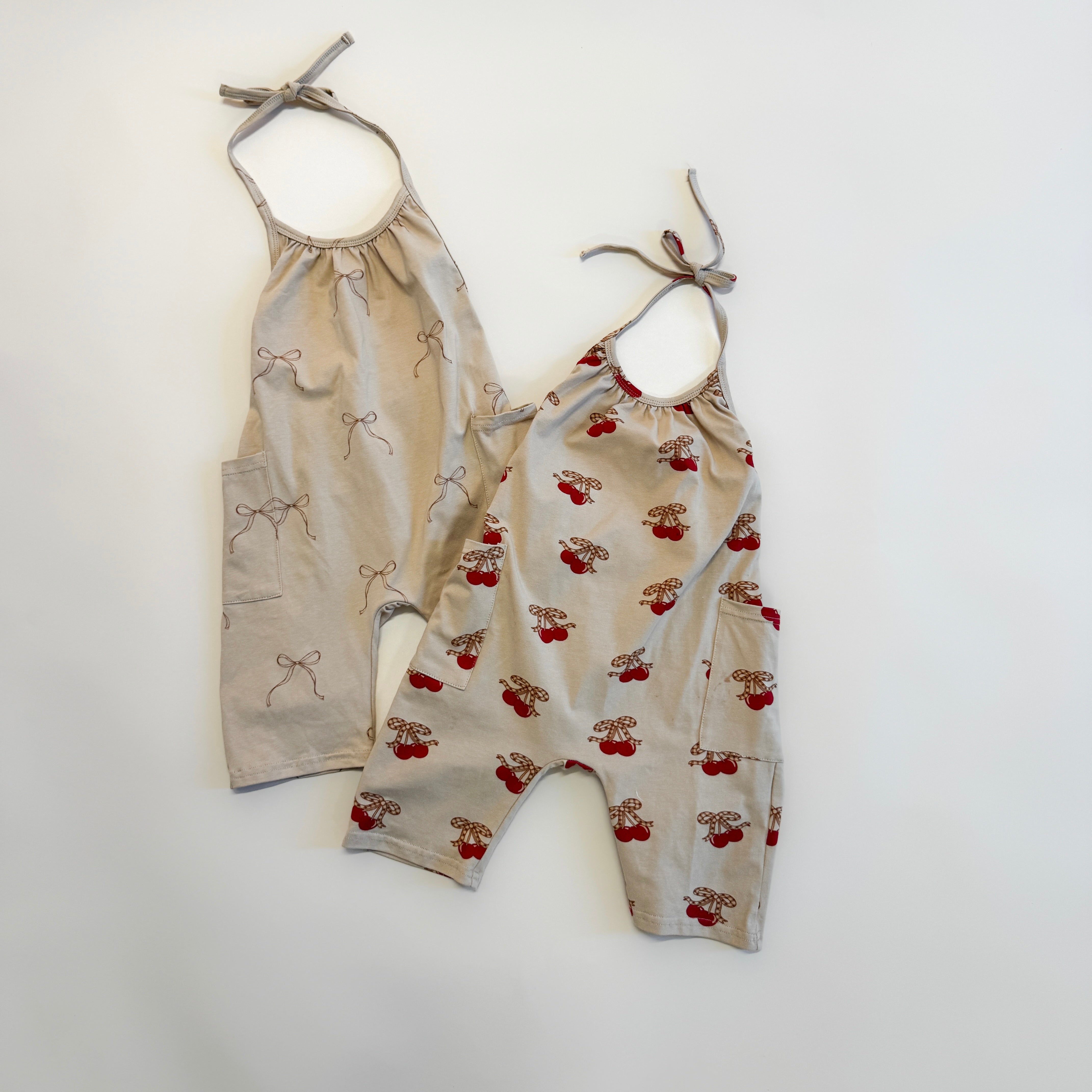 Two cute halter jumpsuit girls in beige with bows and playful patterns, perfect for summer playdates.