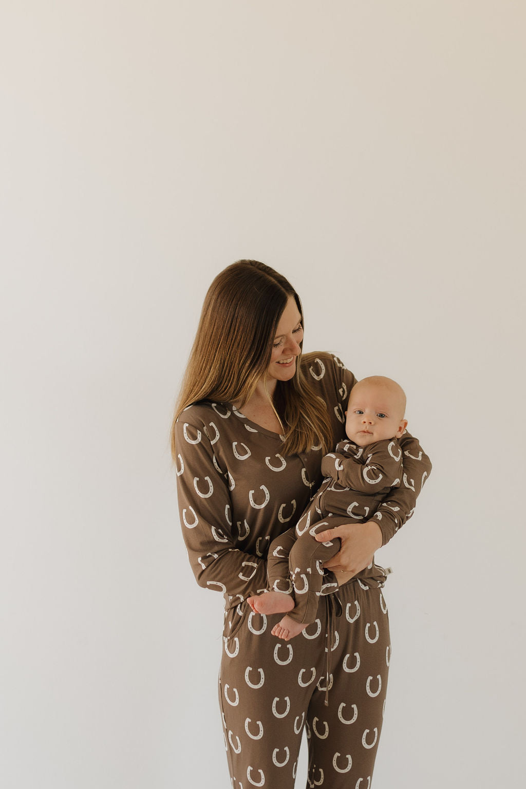 Woman holding a baby, both dressed in womens bamboo pajama giddy up set with a brown horseshoe print.