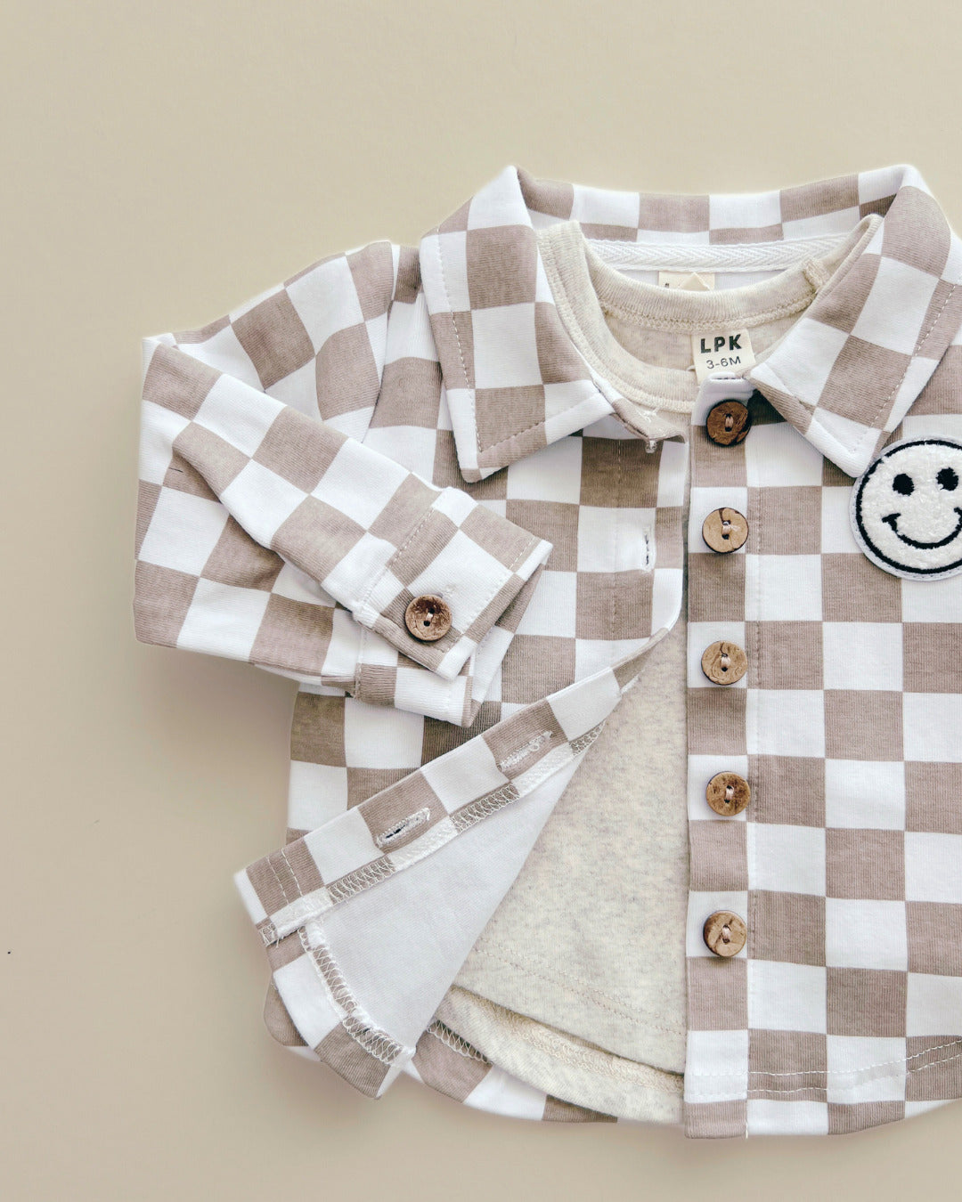 Cotton Shacket in Smiley Checkered Latte with button-down front and playful smiley patch on a neutral background.