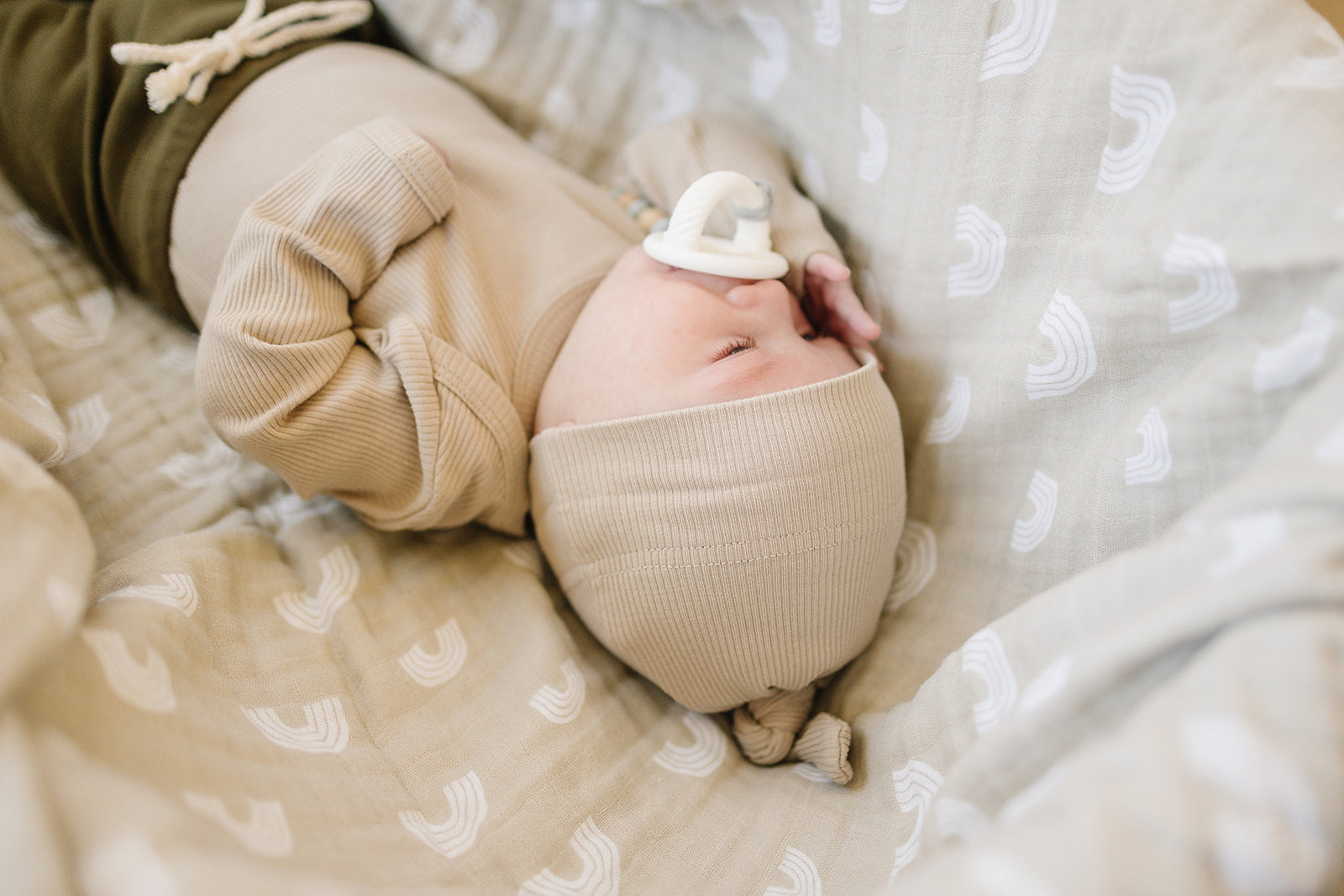Newborn baby wearing an organic ribbed knot hat, sleeping peacefully on a soft patterned blanket.