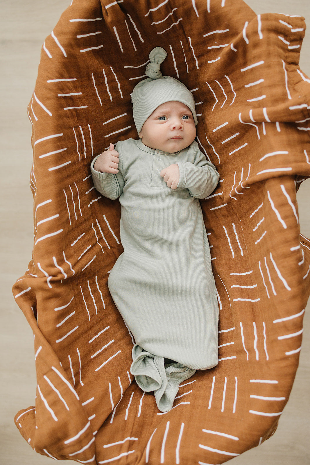 Organic newborn knot hat in sage on baby lying in a brown patterned swaddle blanket.