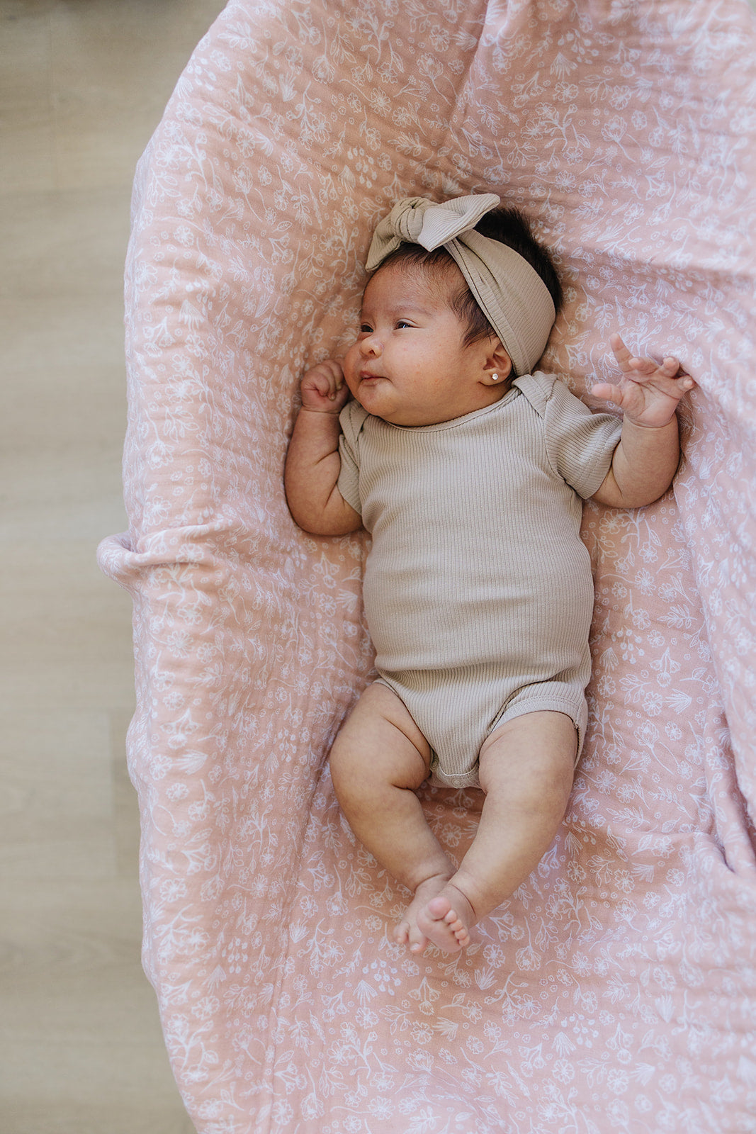 Baby wearing oatmeal organic cotton ribbed head wrap, lounging on a pink floral blanket.