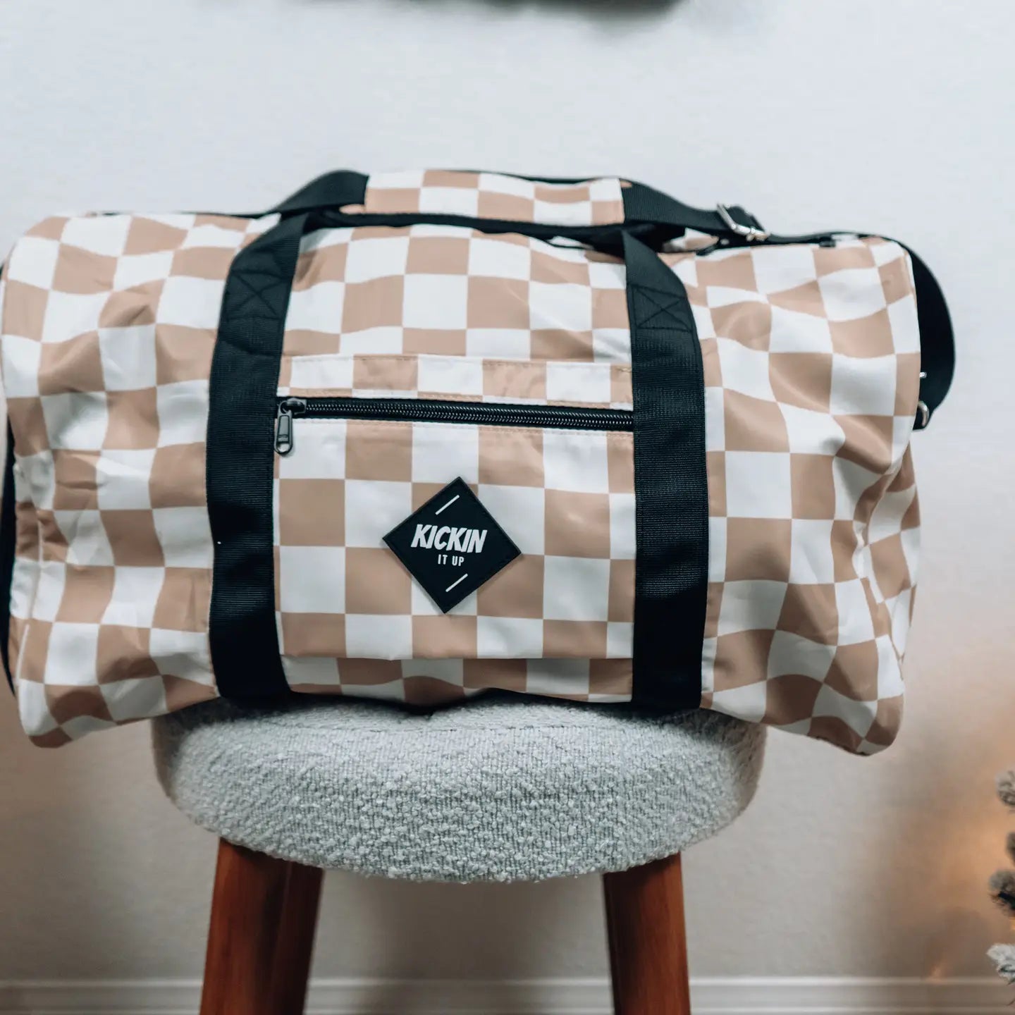 Tan Check Weekender travel bag on a chair, featuring a stylish checkered pattern and durable construction.