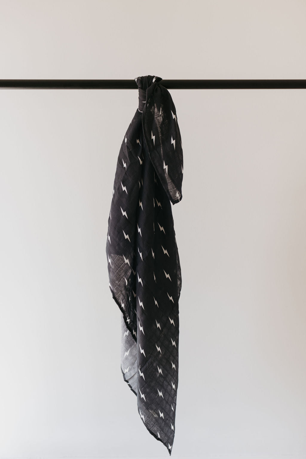 Muslin swaddle midnight lightning bolt hanging on a black rod, showcasing its stylish black-and-white lightning bolt pattern.