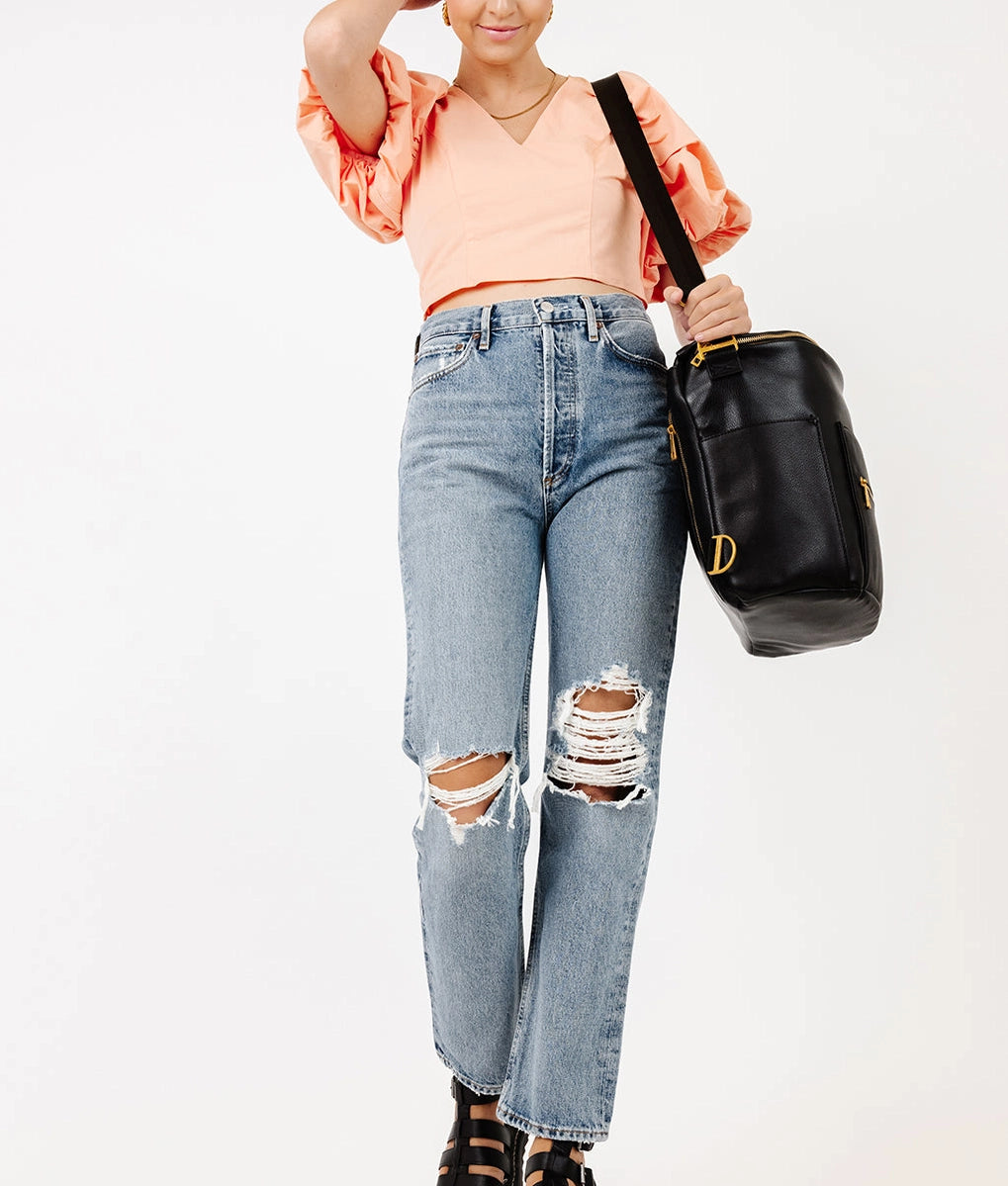 Woman wearing a trendy orange top and ripped jeans, carrying an Original Diaper Bag Backpack in black.