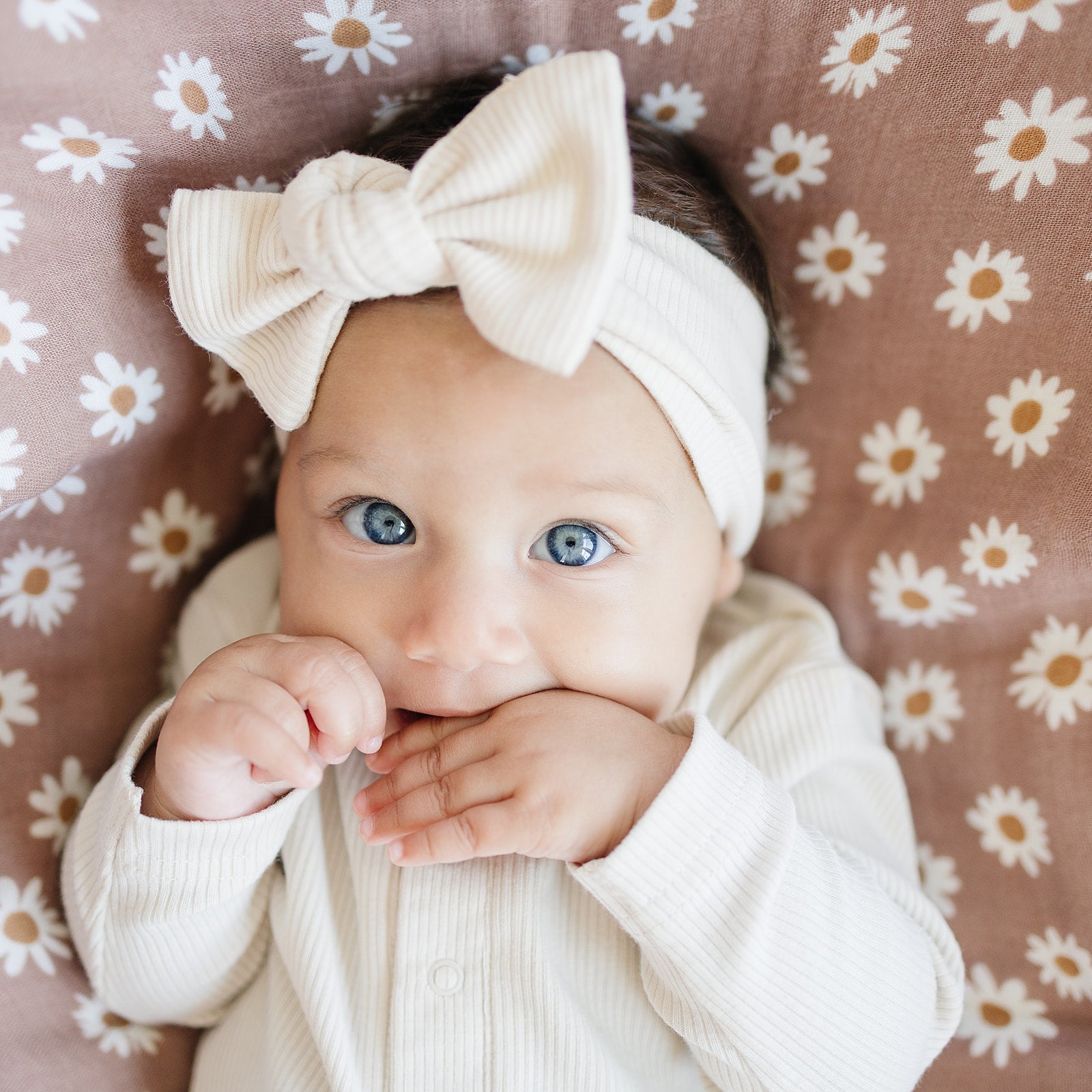Baby wearing a vanilla organic cotton ribbed head wrap with a bow, lying on a floral blanket.