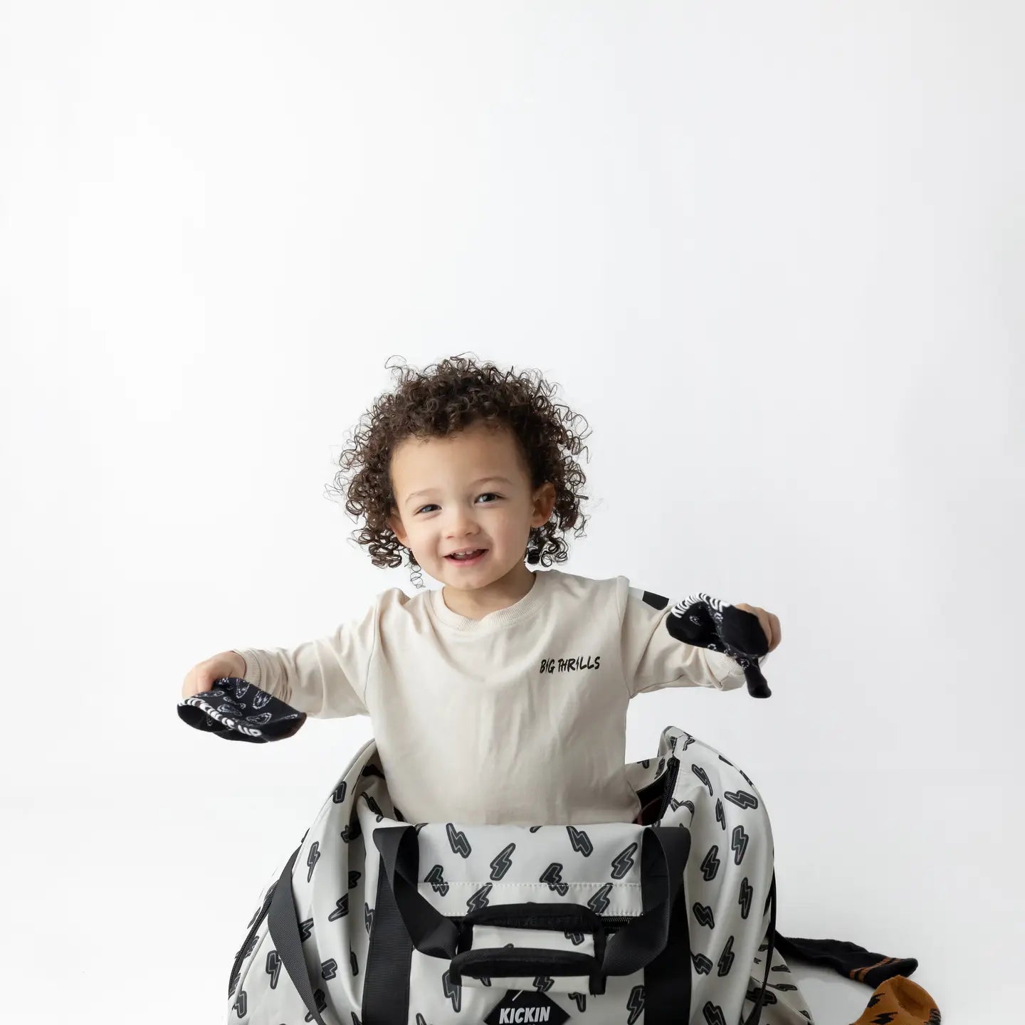 Happy child playing with bags, promoting the Sand Thunderbolt Weekender go-bag for travel and fun.
