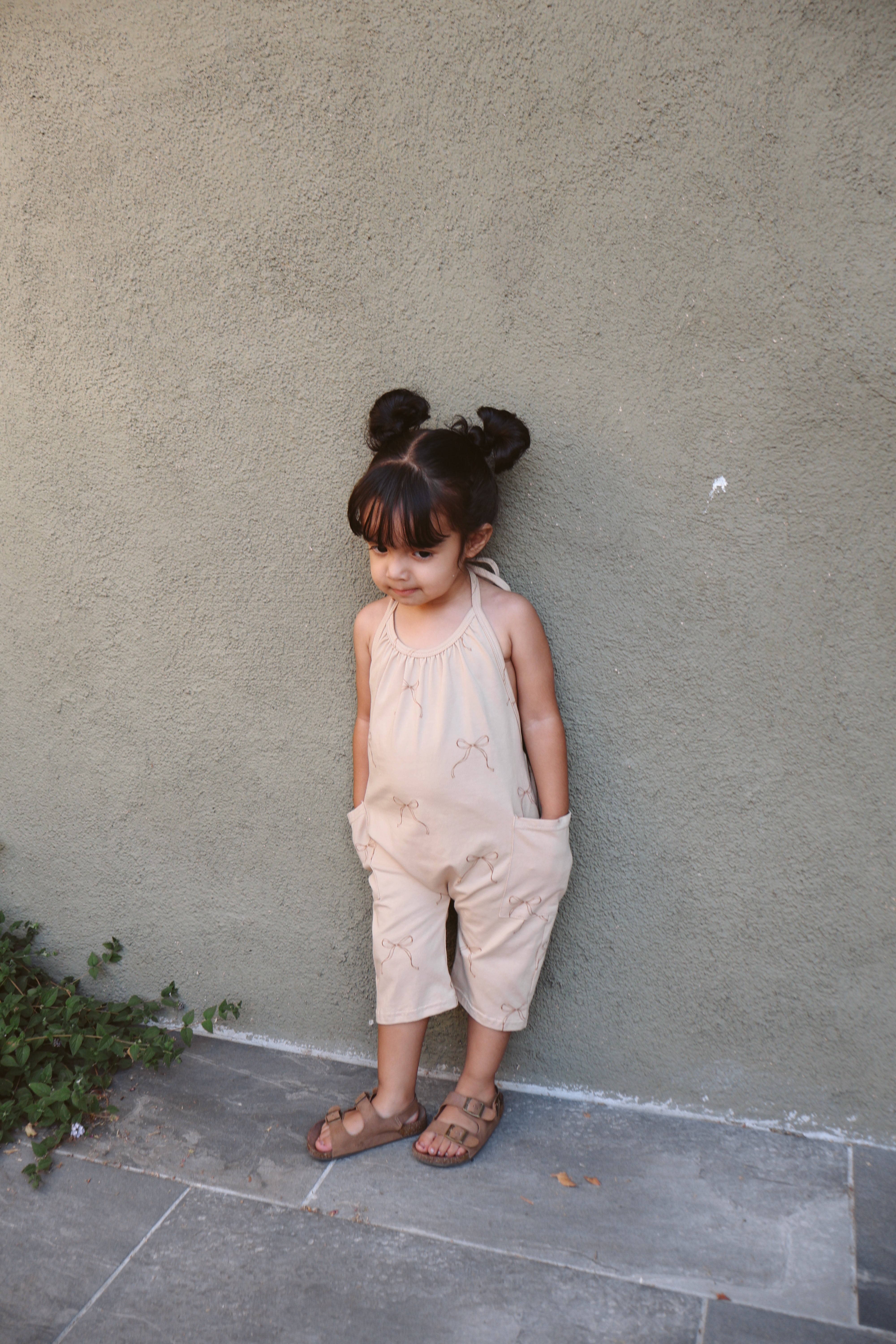 Girl wearing a halter jumpsuit, posing against a wall, perfect for summer playdates and family outings.