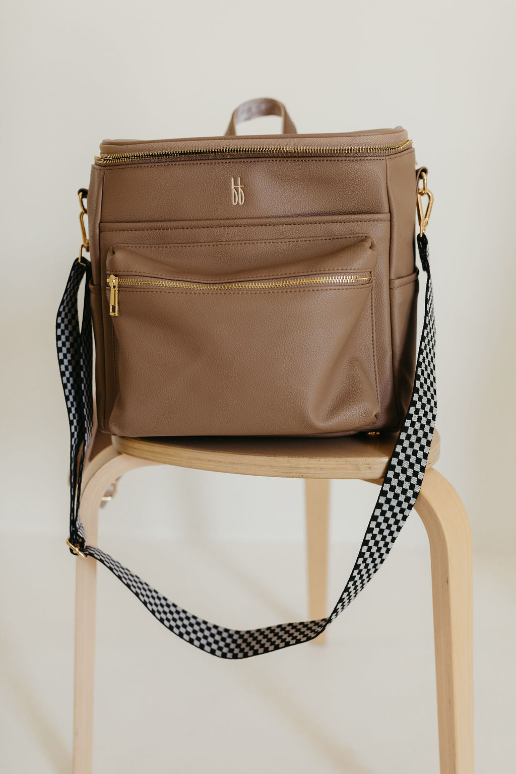 ff Diaper Bag Taupe - Vegan Leather Carry-All on a chair with checkerboard strap.
