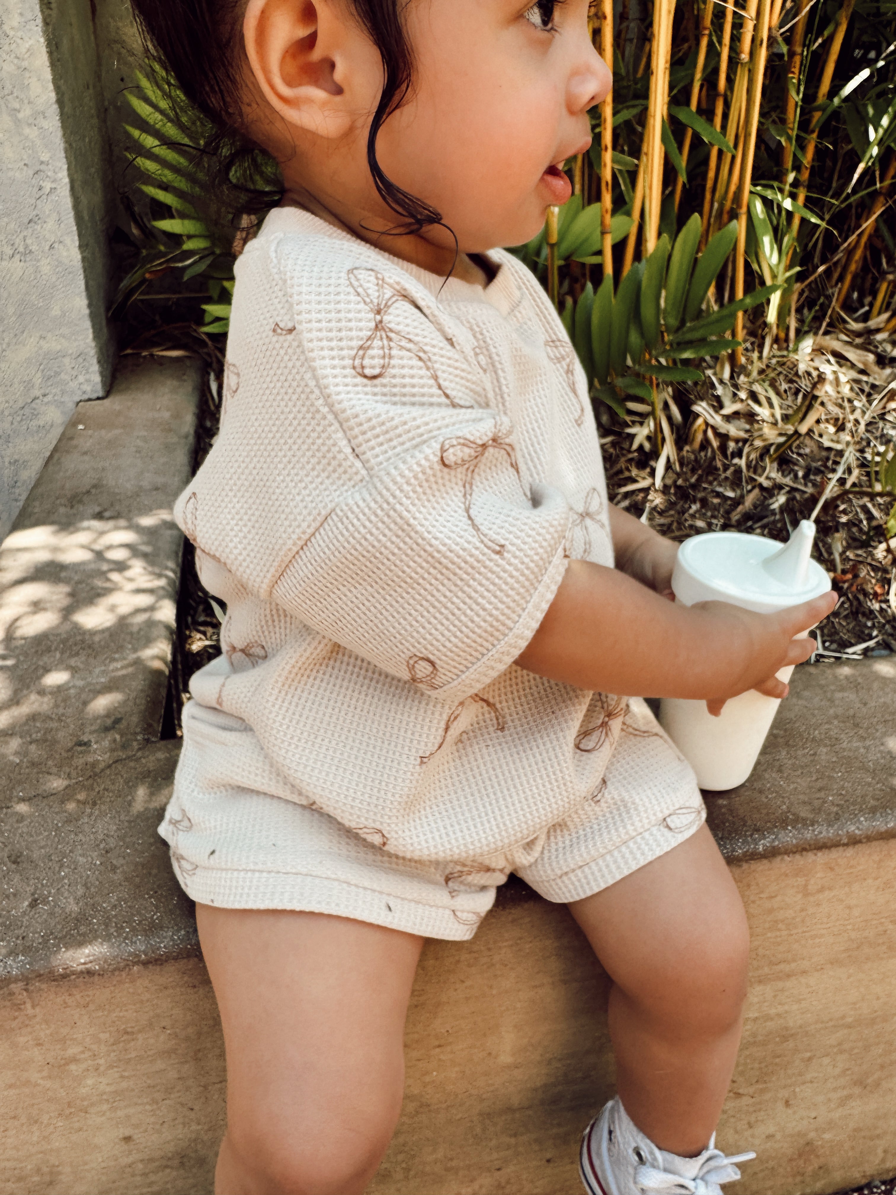 Toddler wearing a comfy printed waffle set in light color with playful design, enjoying a drink outdoors.