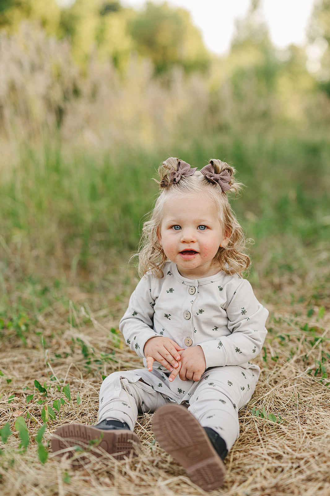 Baby girl in floral button romper sitting on grass, showcasing the cozy and cute style perfect for fall.