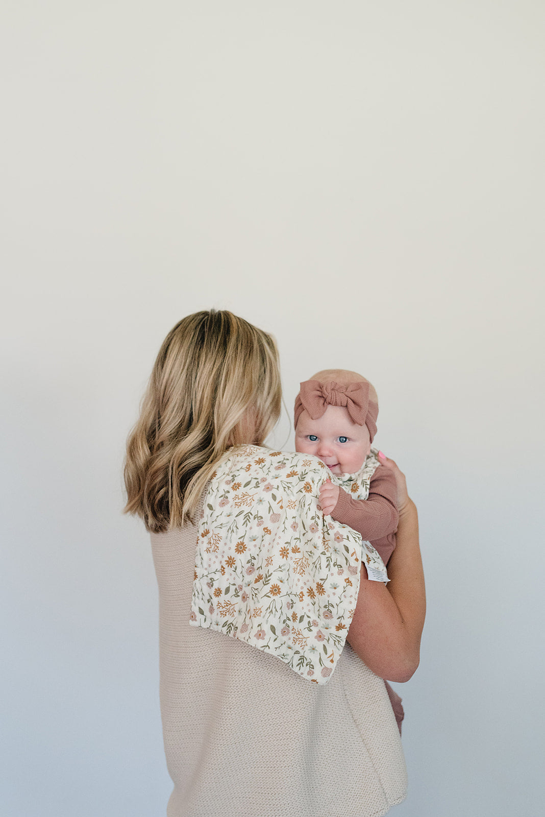 Organic baby head wrap in dusty rose color, worn by a baby held by a woman, showcasing soft ribbed cotton and floral blanket.