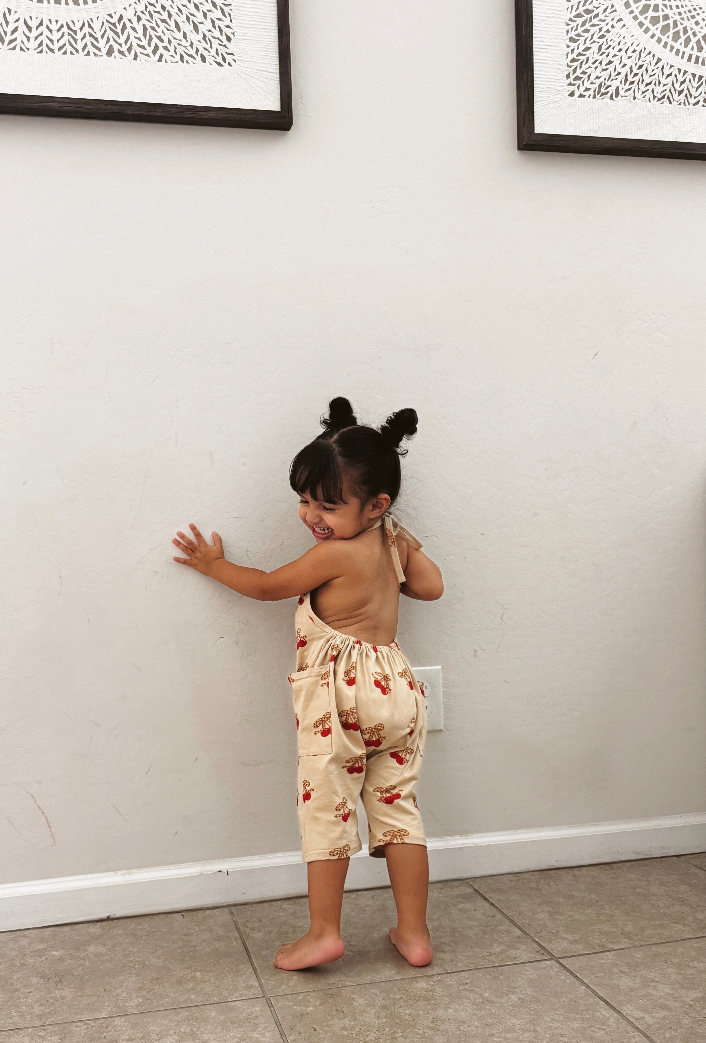 Cute girl in a halter jumpsuit, playfully showing off her outfit against a wall, ideal for summer fun.