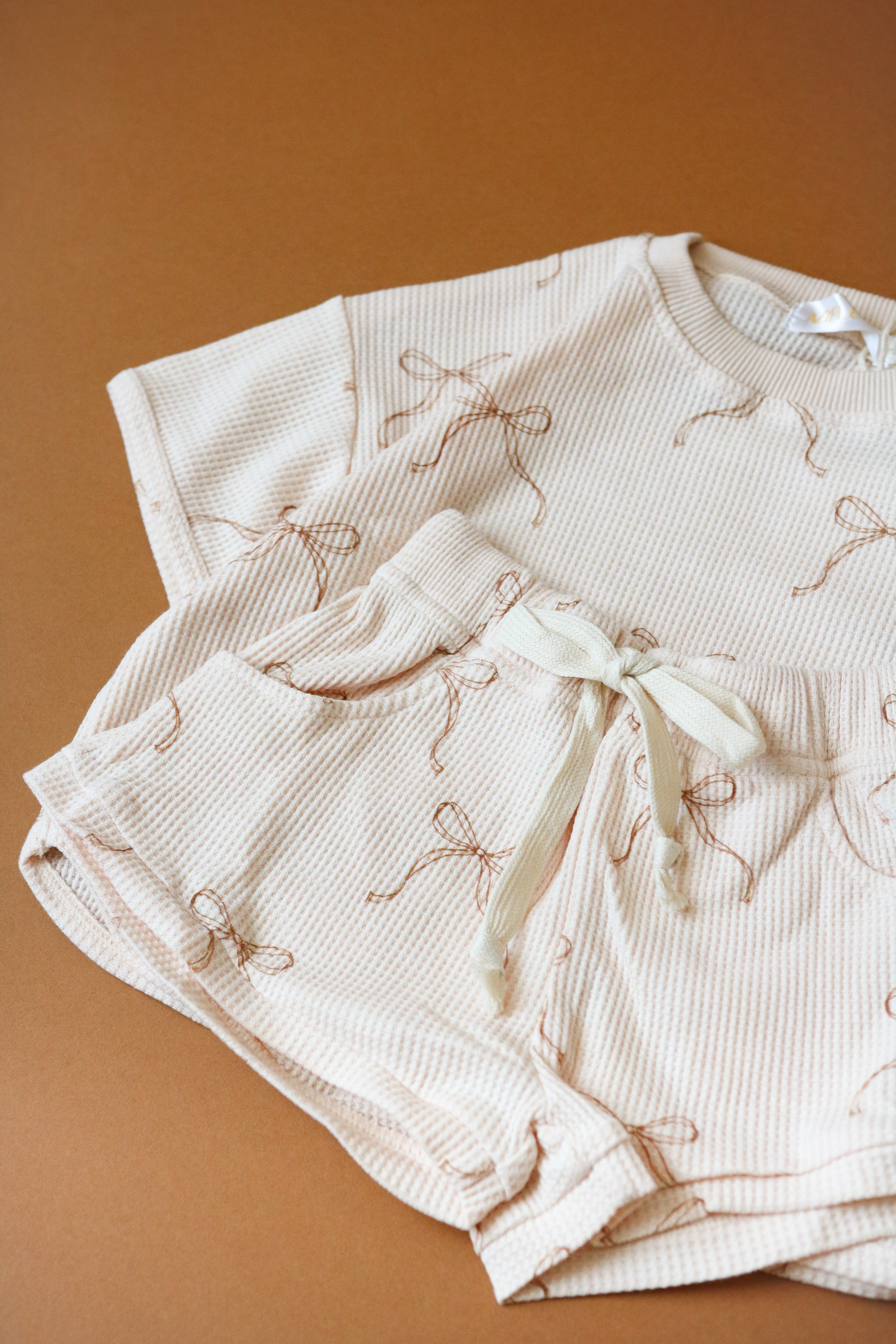 Printed waffle sets kids featuring a beige tee and shorts with playful bow prints, perfect for summer adventures.