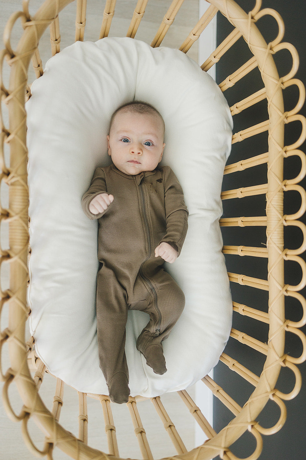 Baby in cocoa organic cotton ribbed pajamas lying in a cozy bassinet. Ideal for comfort and easy diaper changes.