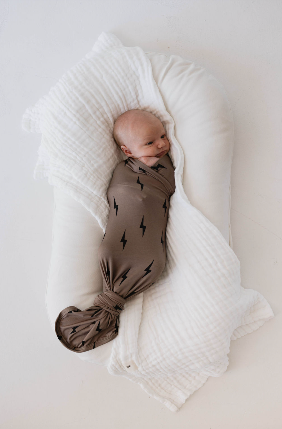 Baby wrapped in Bamboo Swaddle Black and Brown Lightning Bolt with white blanket.