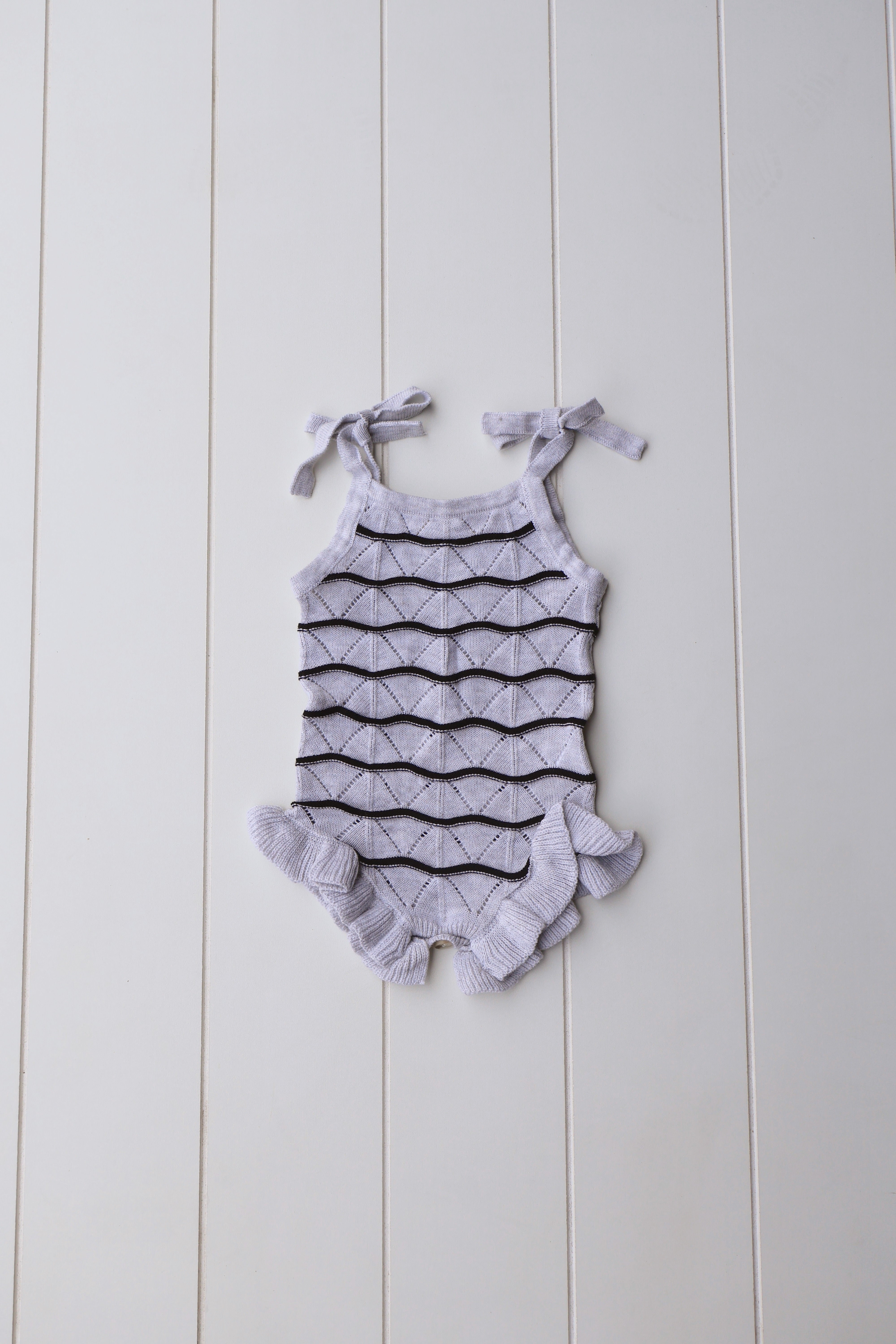 Spring Knit Ruffle Onesie for baby girls with ruffle details and adjustable straps on a light background.