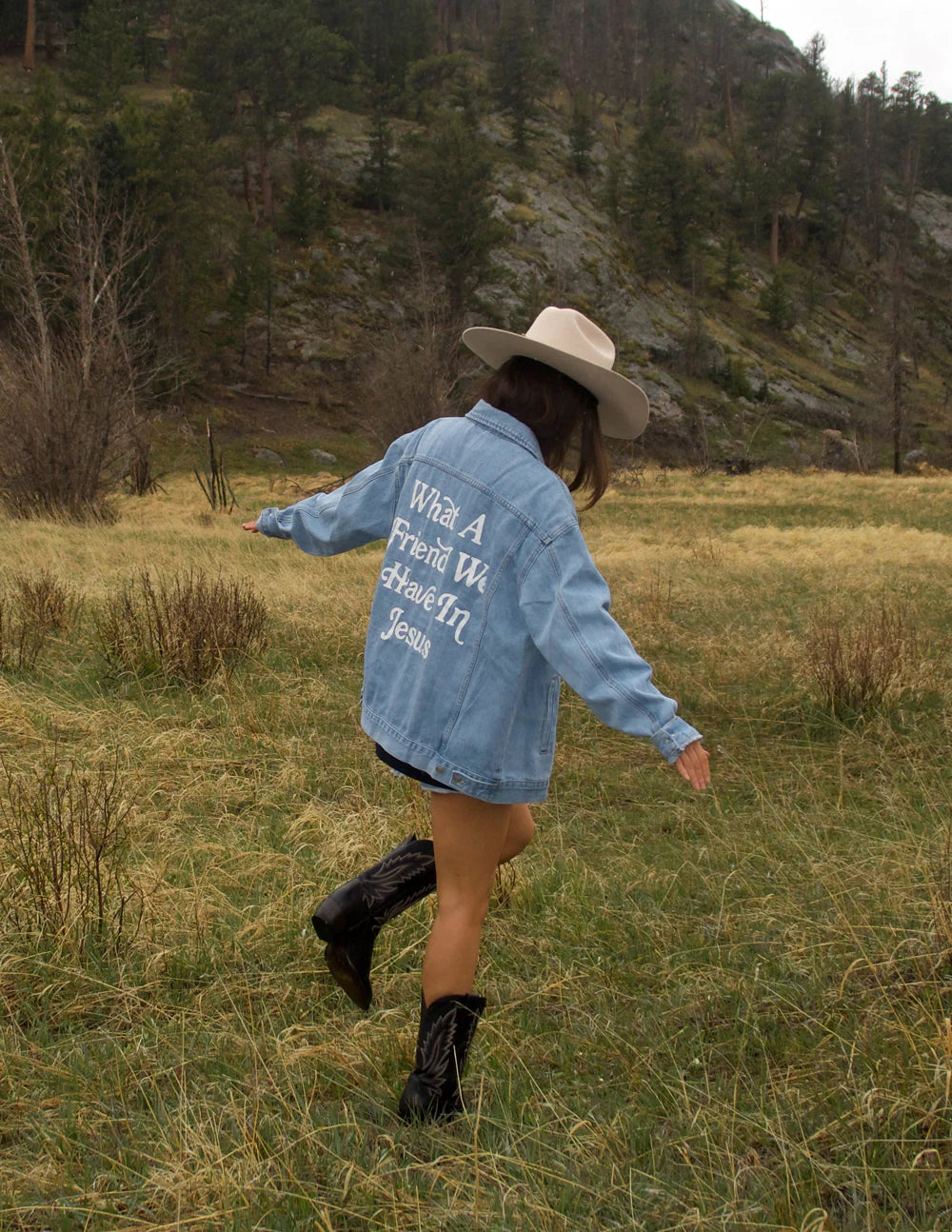 Woman wearing What a Friend in Jesus Denim Jacket in a grassy field, showcasing a relaxed fit and faith-inspired message.