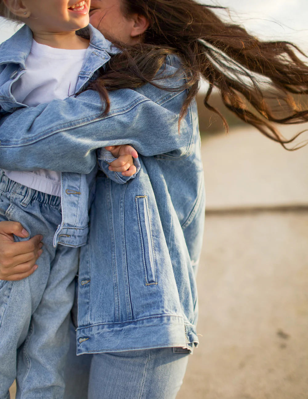 Mom and child joyfully wearing matching what a friend in Jesus kids denim jackets, embracing in the sunlight.