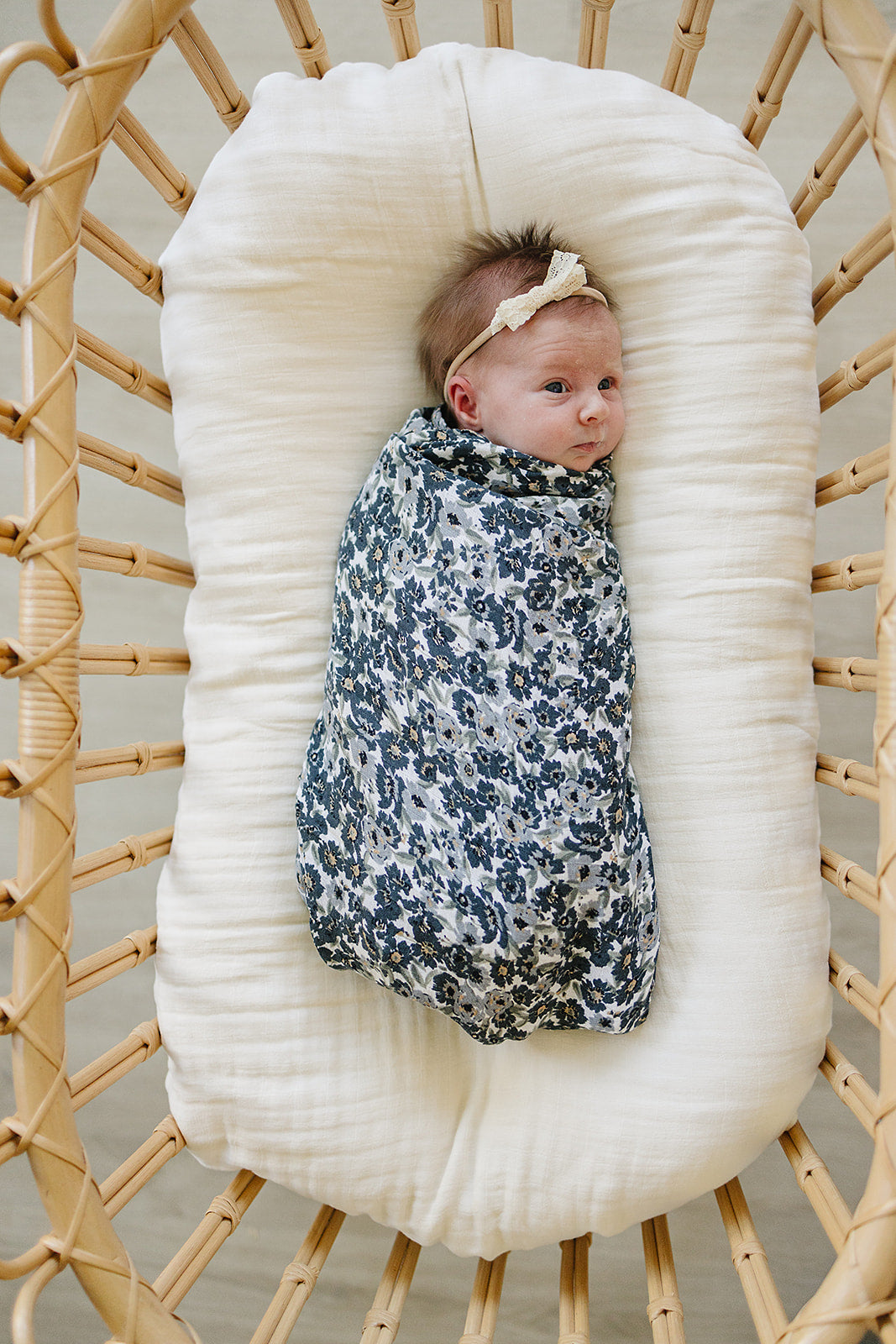 Baby wrapped in a Muslin Swaddle Blanket – Liberty Floral, featuring a floral design in a cozy bassinet.