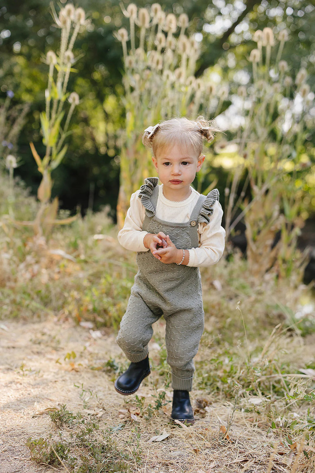 Toddler girl wearing green ruffle knit overalls in a natural outdoor setting, perfect for playtime or photos.