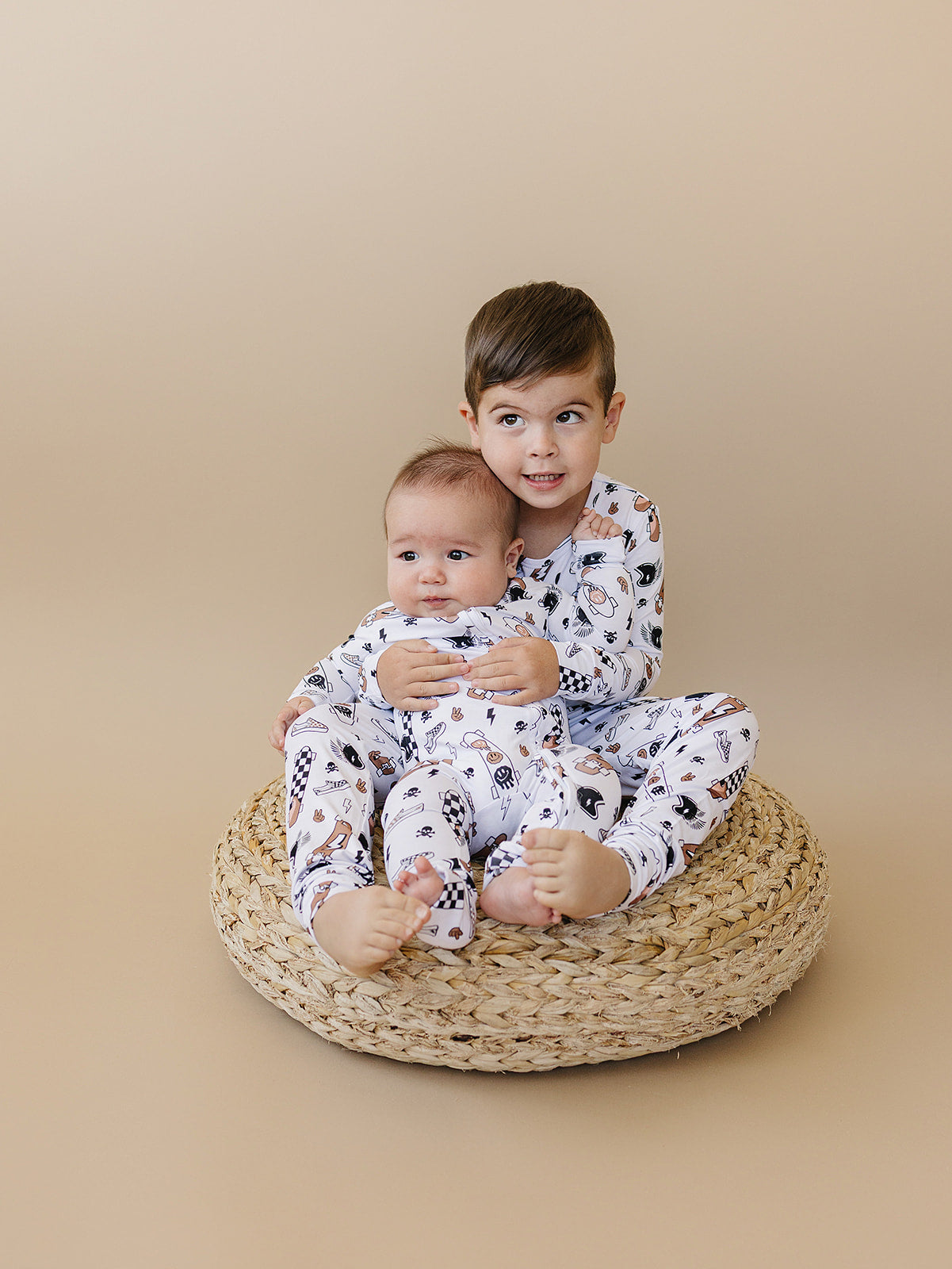 Two children wearing the Bamboo Two Piece Set Sk8er lounge set sitting on a woven basket.