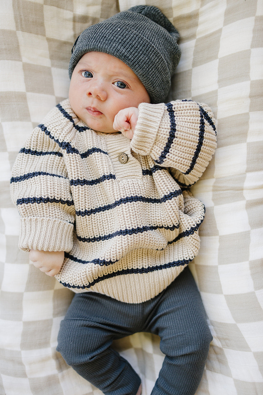 Infant wearing a classic striped knit sweater for babies, featuring navy and cream stripes, paired with a cozy beanie.