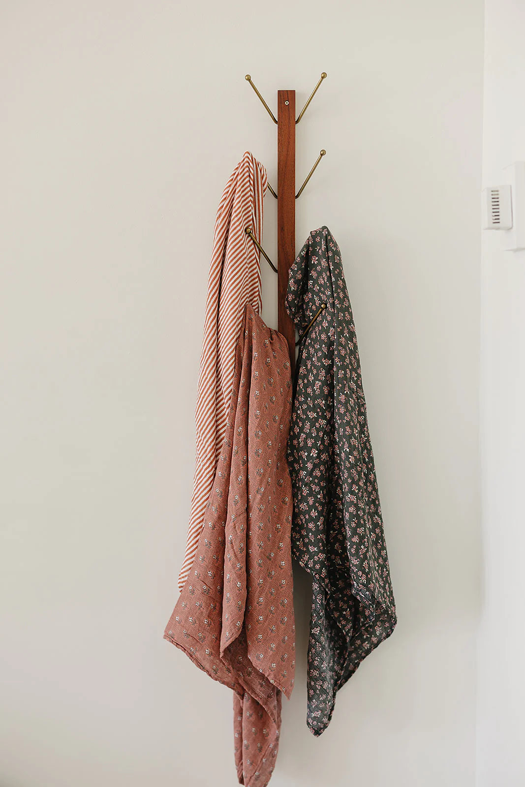 Three beautiful muslin swaddle blankets hanging, featuring pink stripes and floral patterns, showcasing versatility and style.