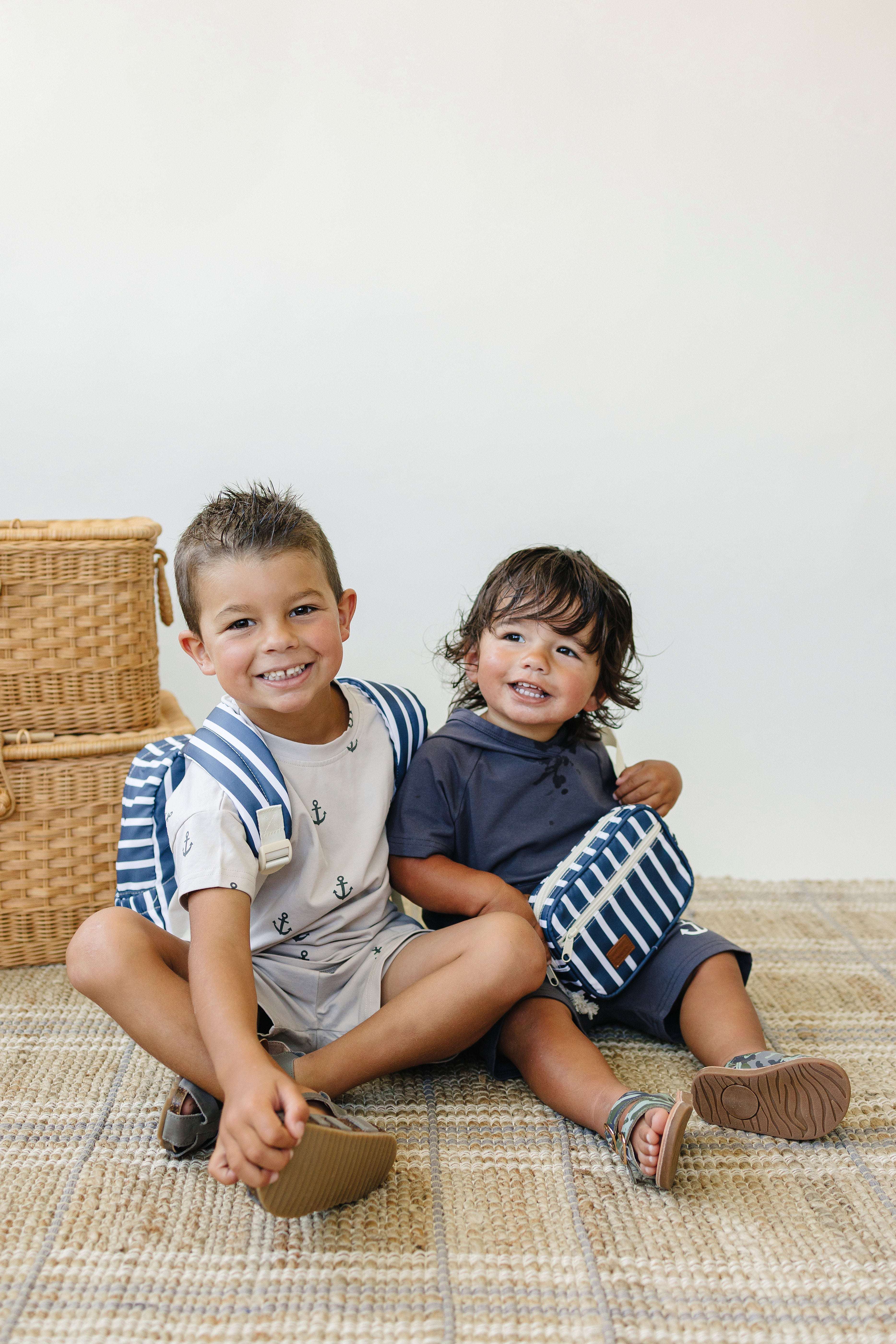 Two kids sitting on a rug, one wearing a navy stripe mini fanny pack, enjoying a playful moment.