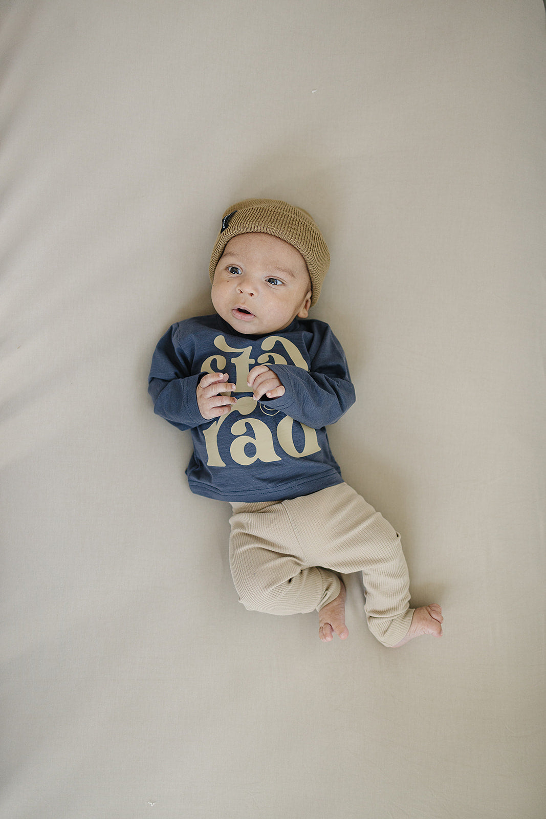 Baby in navy shirt and beige pants, showcasing comfy organic baby leggings and playful style.