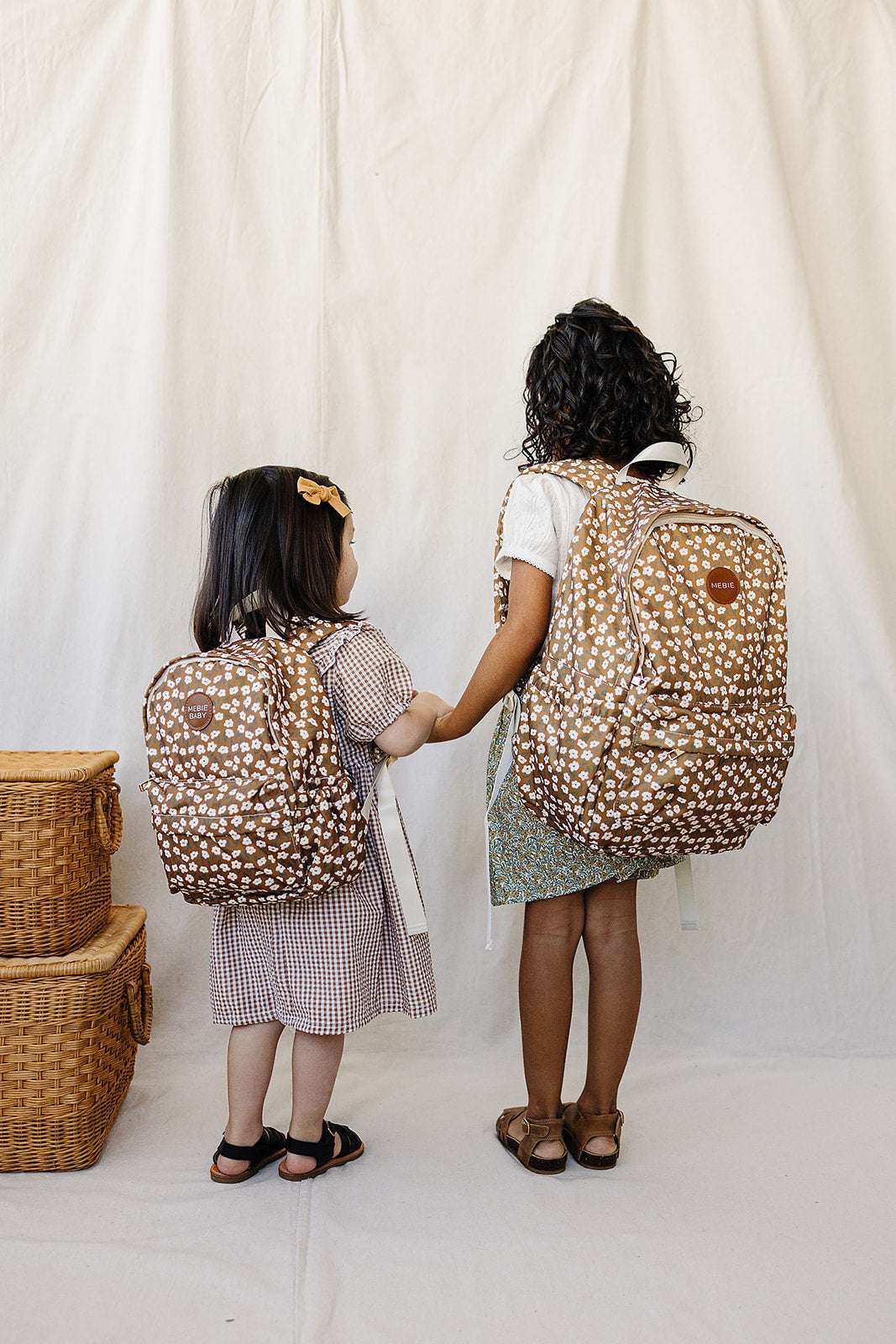 Two kids holding hands, wearing matching floral backpacks, perfect for school and playful adventures.