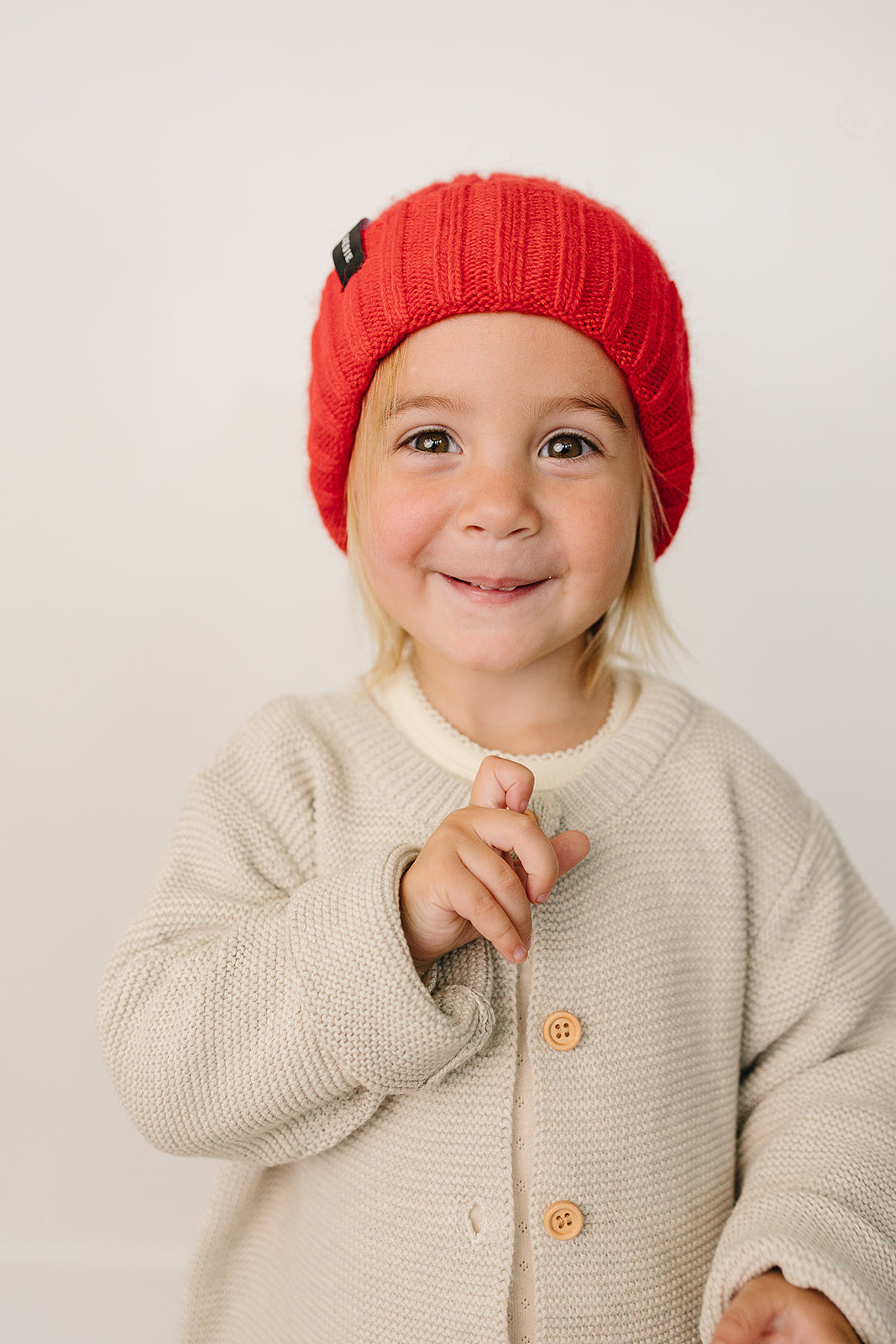 Cute child wearing a bright red baby beanie, smiling and dressed in a cozy outfit.
