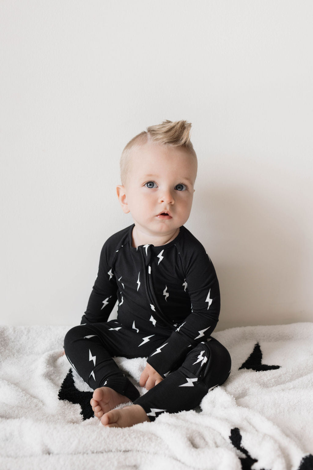 Baby in Bamboo Zip Pajamas with lightning bolt print, sitting on a cozy blanket.
