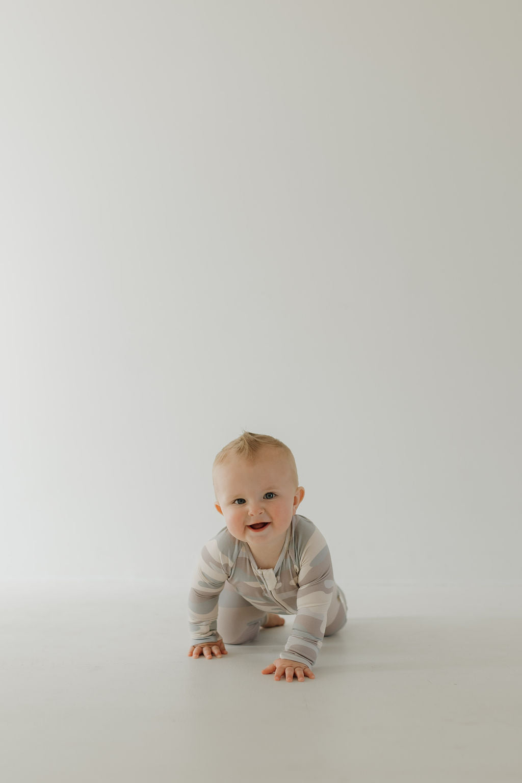 Smiling baby crawling in soft bamboo zip pajamas, showcasing cozy camo print and double zipper functionality.