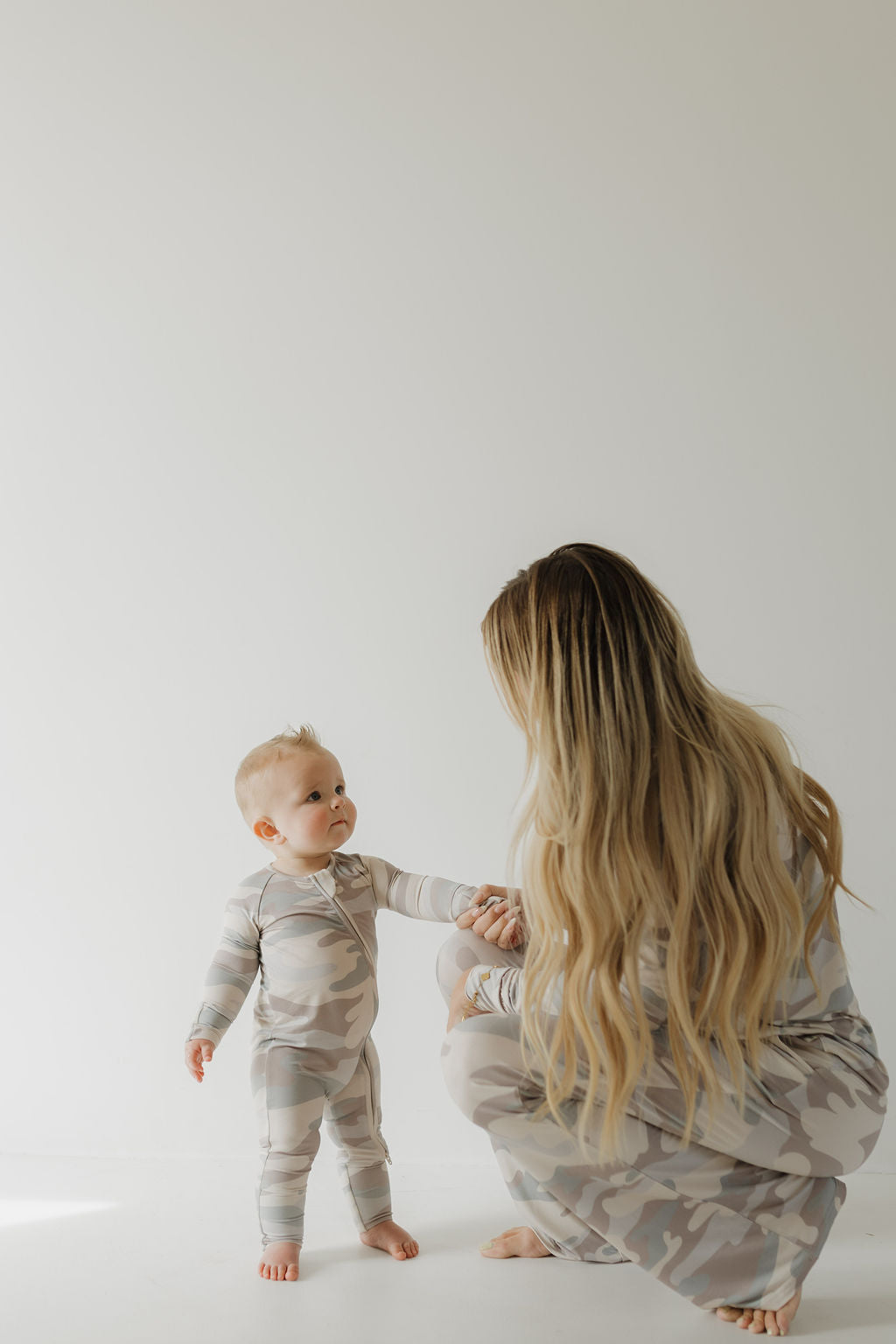 Mom and baby in cozy camo bamboo zip pajamas, showcasing a playful bonding moment.