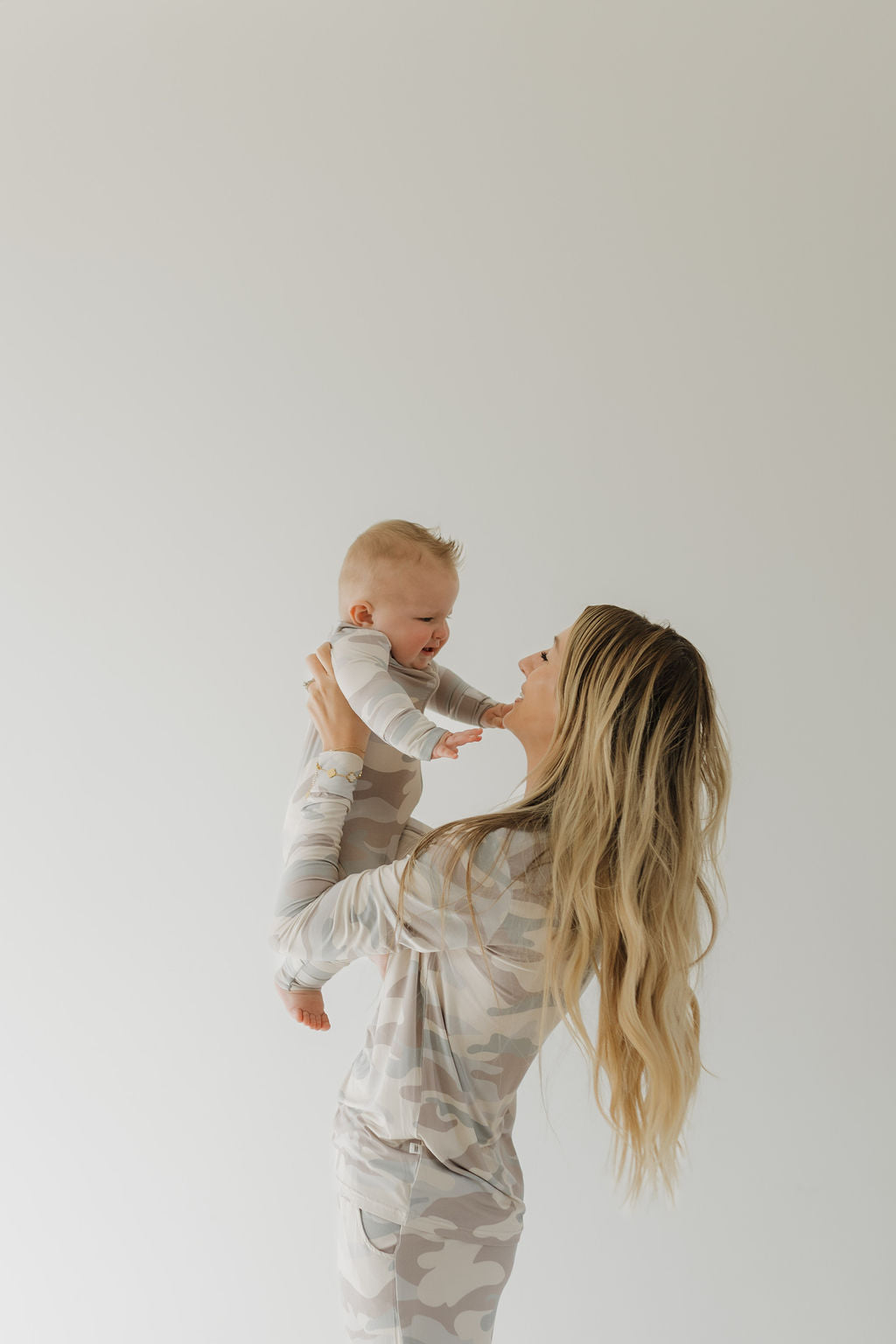 Mom holding baby in soft camo bamboo zip pajamas, showcasing a cozy and stylish parenting moment.
