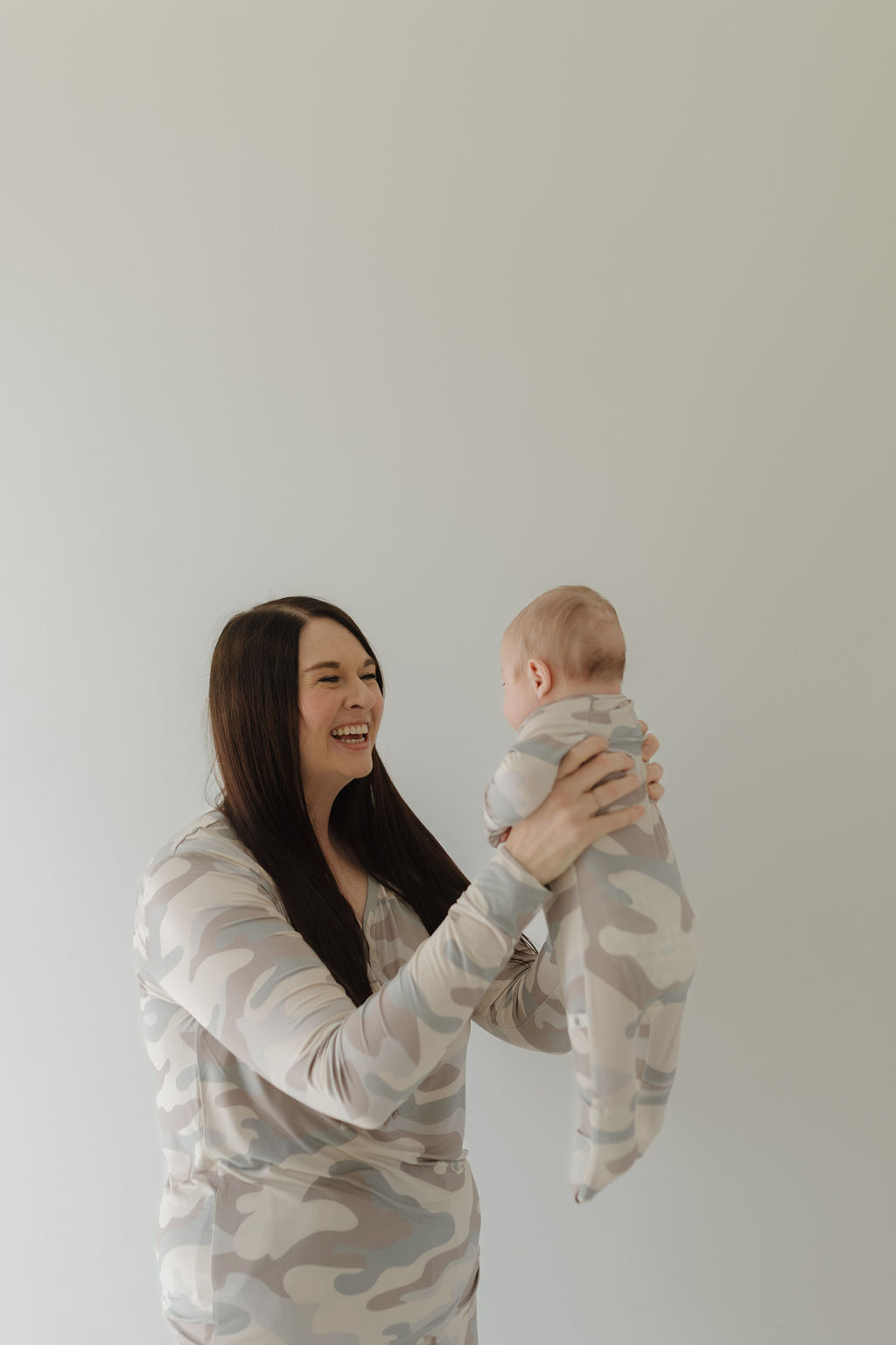 Parent joyfully holding baby in matching neutral camo zip pajamas, showcasing cozy and stylish design.