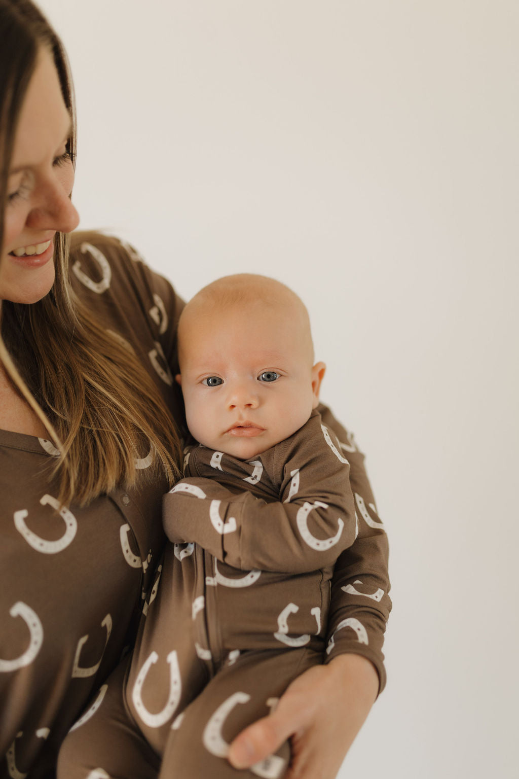 Mom holding baby in matching western-themed pajamas with horseshoe print.
