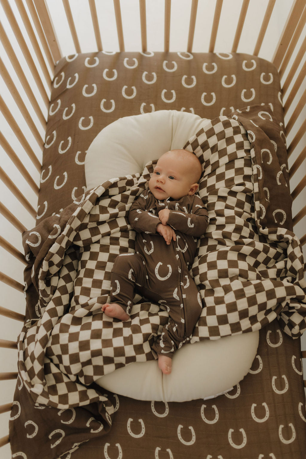Baby in bamboo zip pajamas on a cozy crib sheet with a brown checkered pattern and horseshoe design.