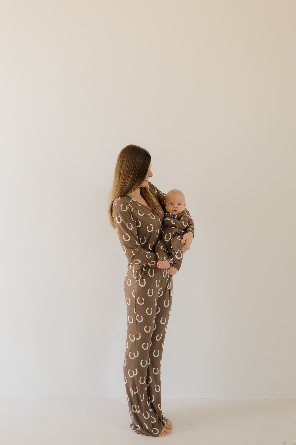 Woman in matching bamboo pajamas holding baby, both in playful western horseshoe print.
