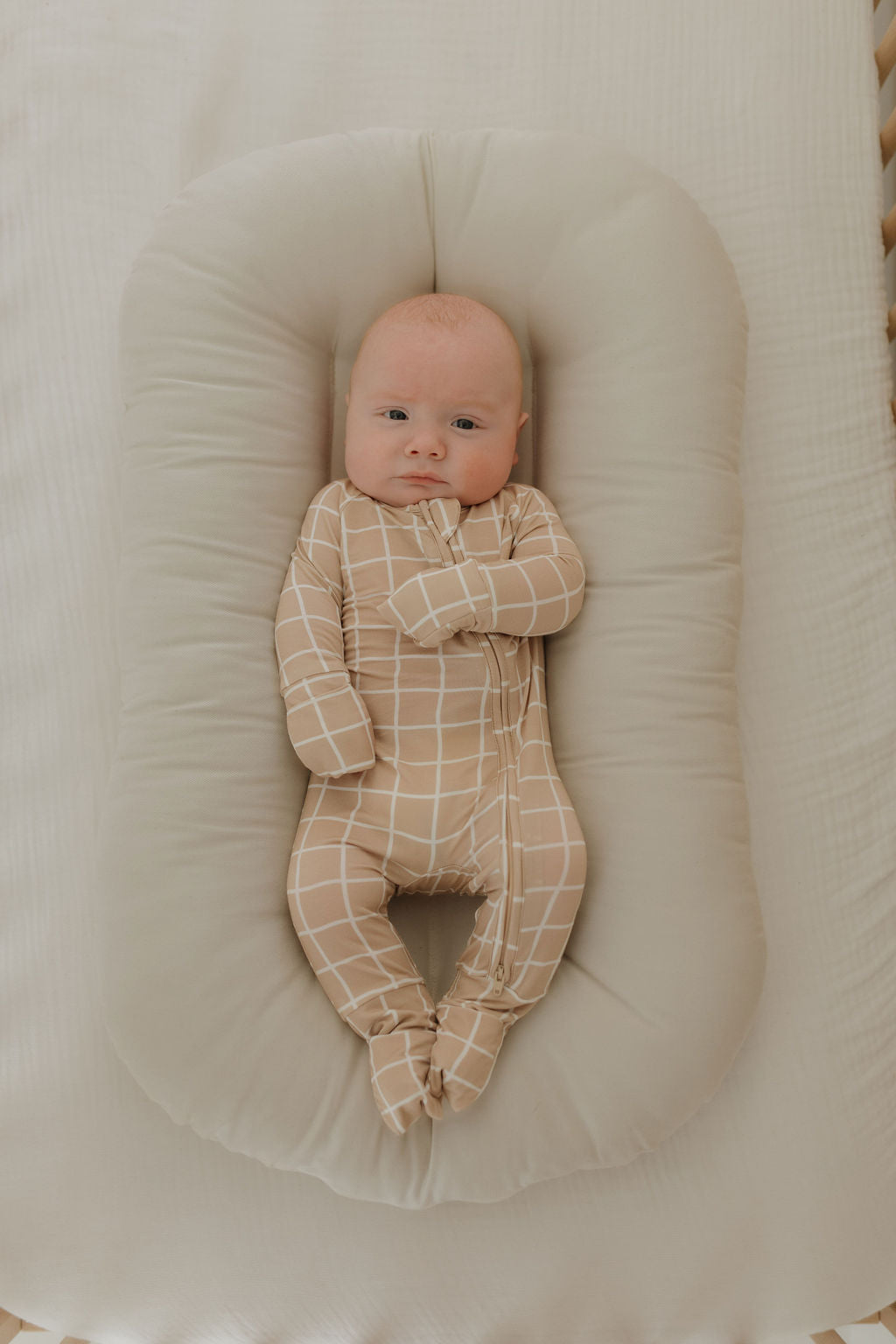Baby wearing grid bamboo zip pajamas on a soft bedding, showcasing the cozy design and stylish print.
