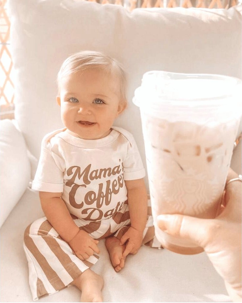 Happy baby in striped outfit smiling while holding iced coffee, perfect for a cozy family moment.
