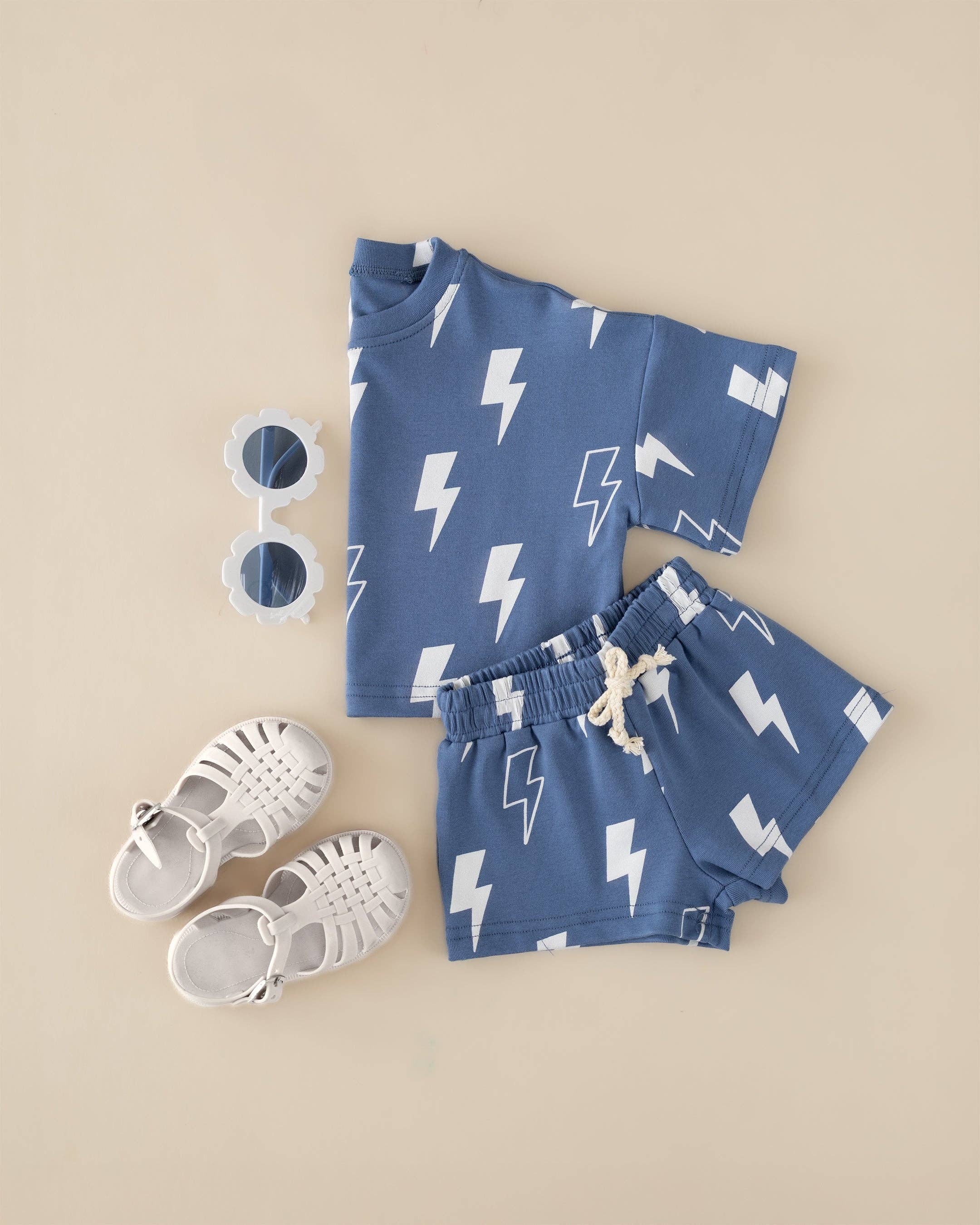 Blue Bolts toddler shorts set featuring a lightning print tee and shorts, paired with white sandals and sunglasses.