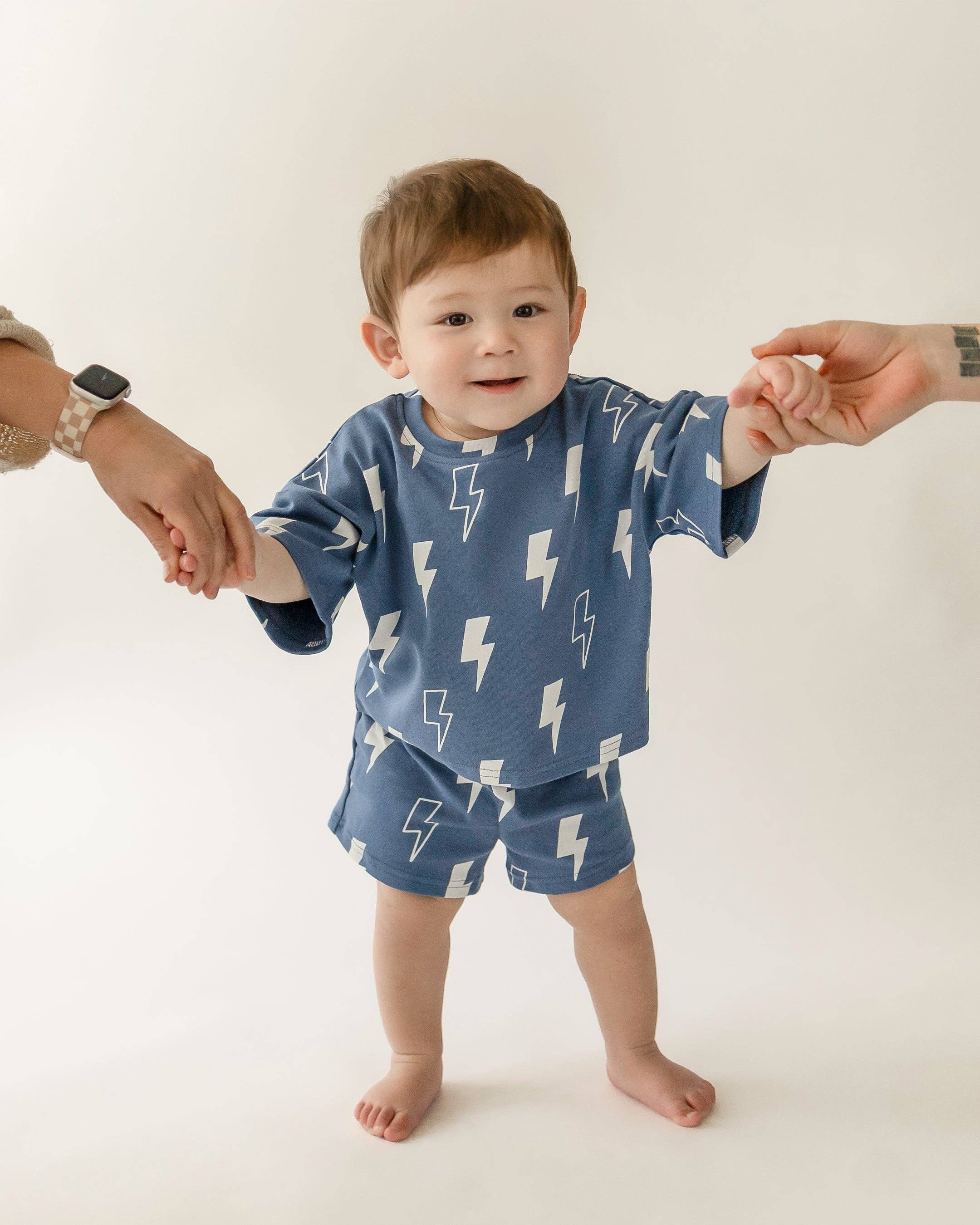 Toddler wearing Blue Bolts shorts set with lightning bolt print, held by adults, perfect for playtime.