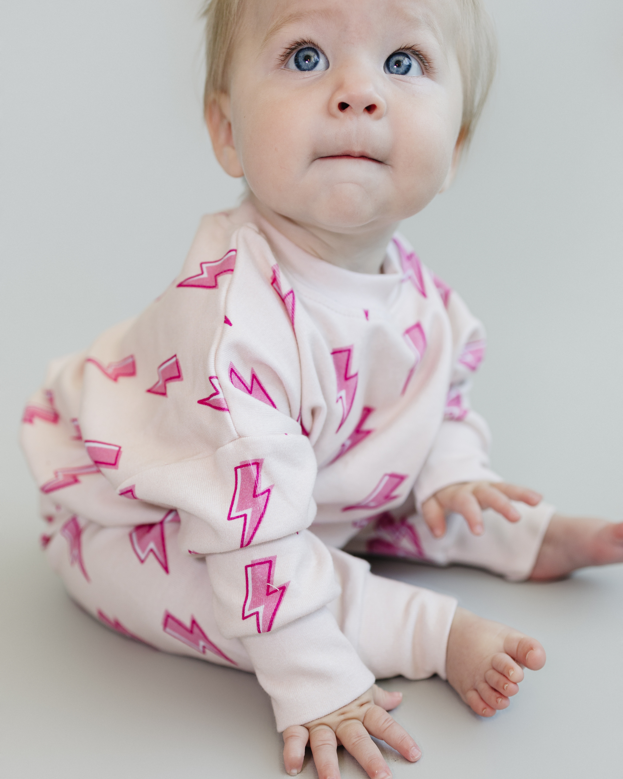 Toddler wearing pink bolt jogger set, featuring lightning bolt print, sitting and looking up, showcasing comfy kids loungewear.