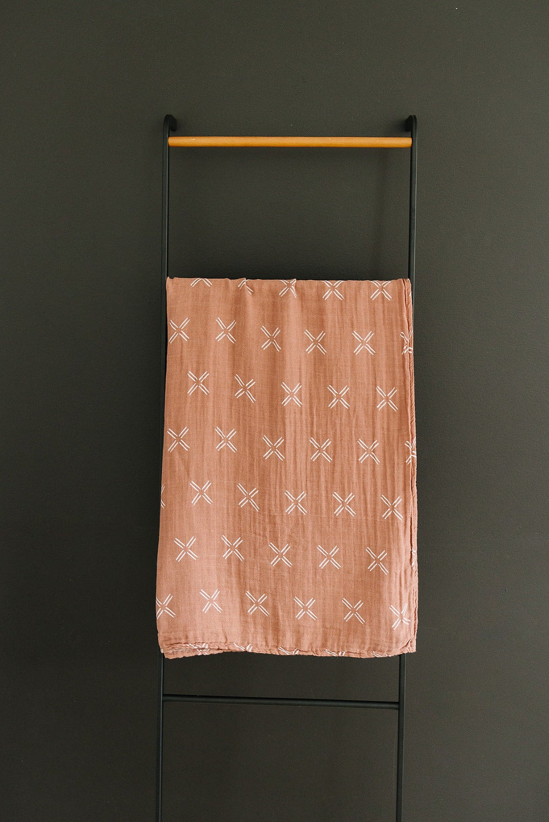 Muslin Swaddle Blanket in Just Peachy hanging on a display rack, featuring modern peach print design.