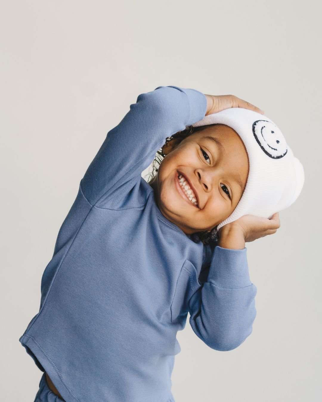 Smiling child wearing a white beanie and ocean blue lounge set, showcasing playful comfort and style.